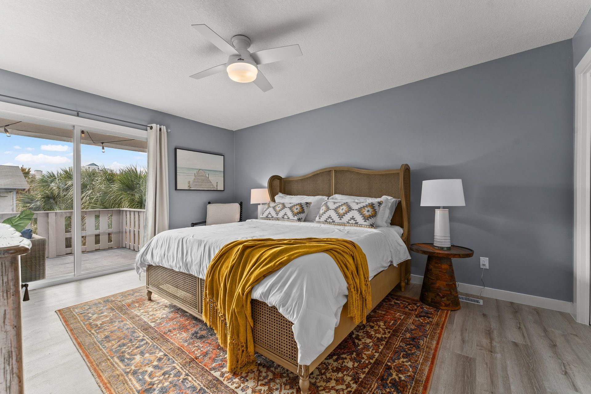 Bright bedroom with a king bed, gray walls, patterned rug, and balcony doors.