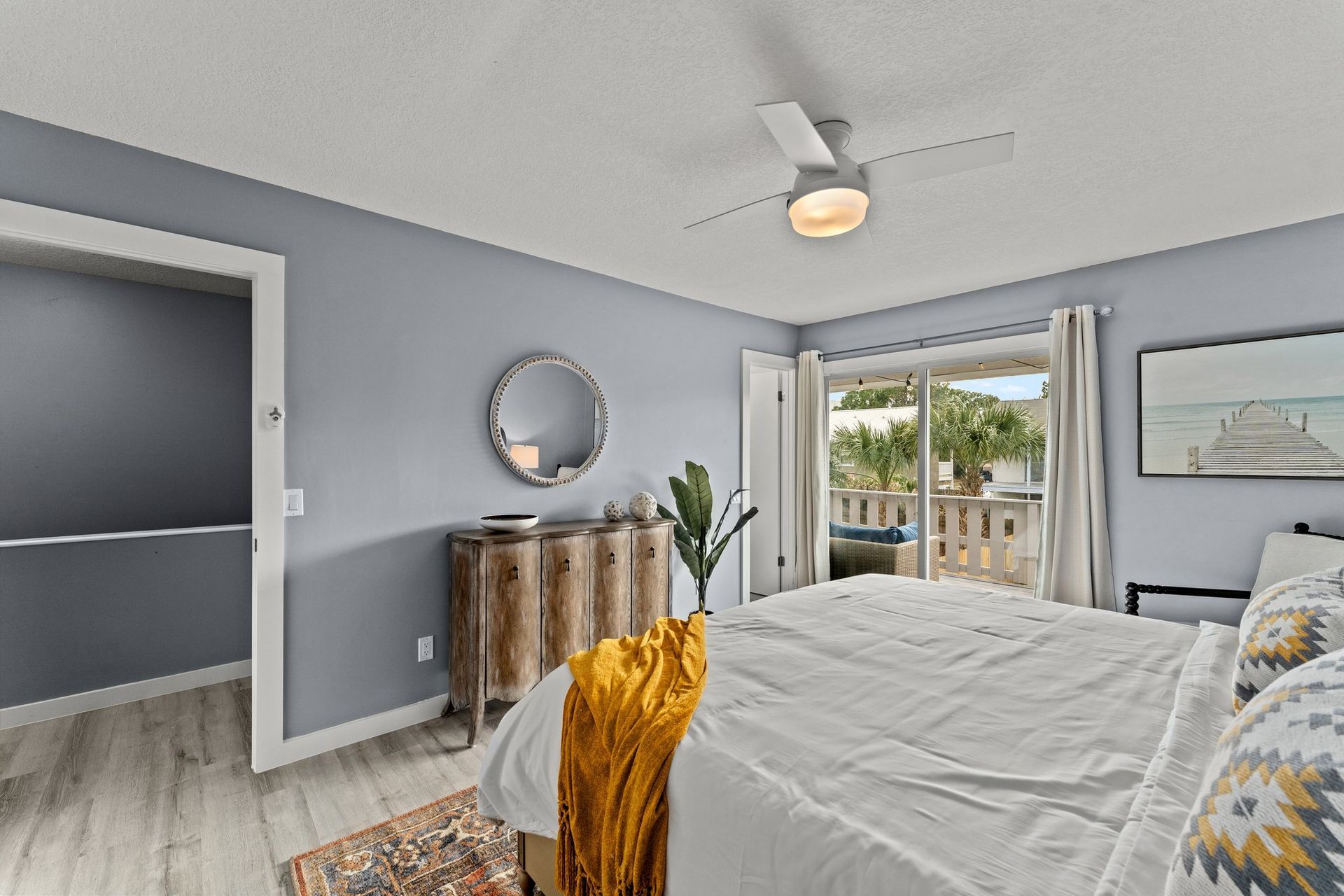 Bright bedroom with gray walls, white bed, wooden dresser, and balcony doors opening to a view outside