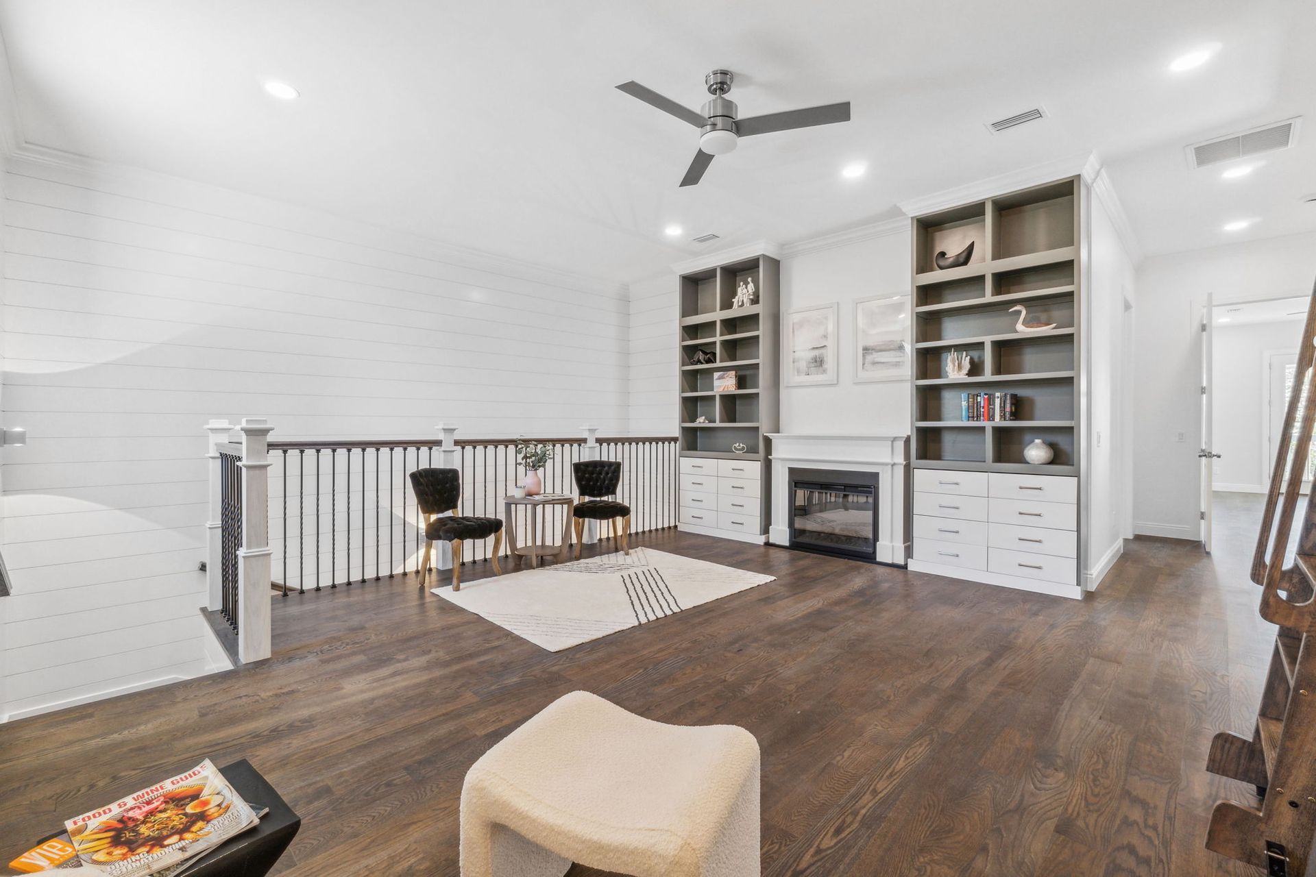 Bright modern living room with built-in shelves, fireplace, hardwood floors, and a small table by a stair railing