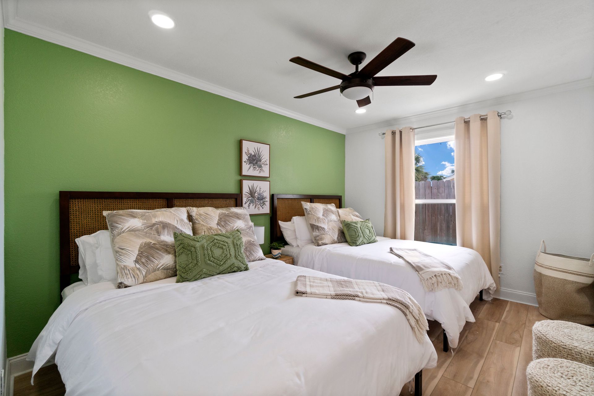 Bright bedroom with two twin beds, green accent wall, ceiling fan, and window with curtains