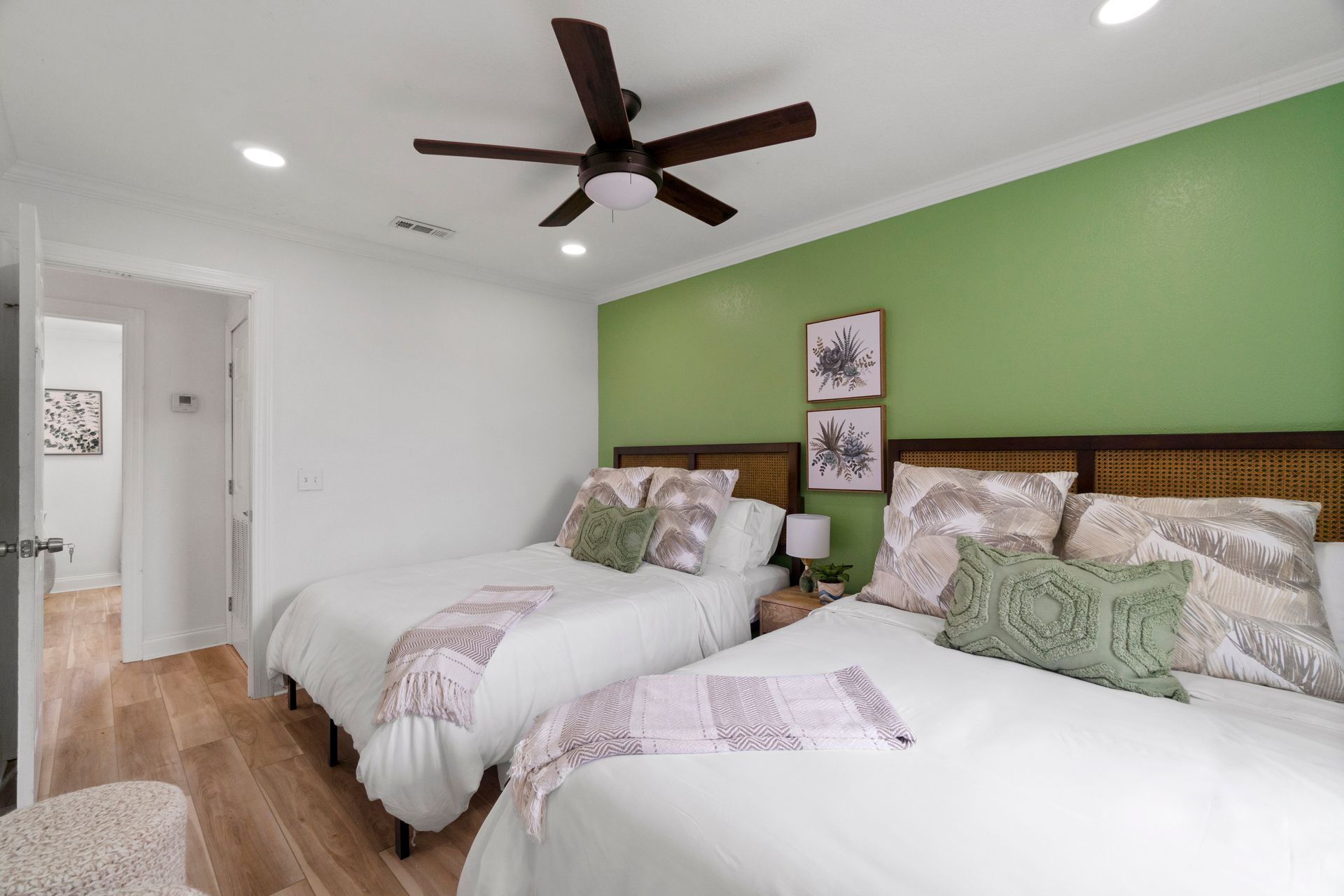 Bright bedroom with green accent wall, two twin beds, ceiling fan, and wood flooring.
