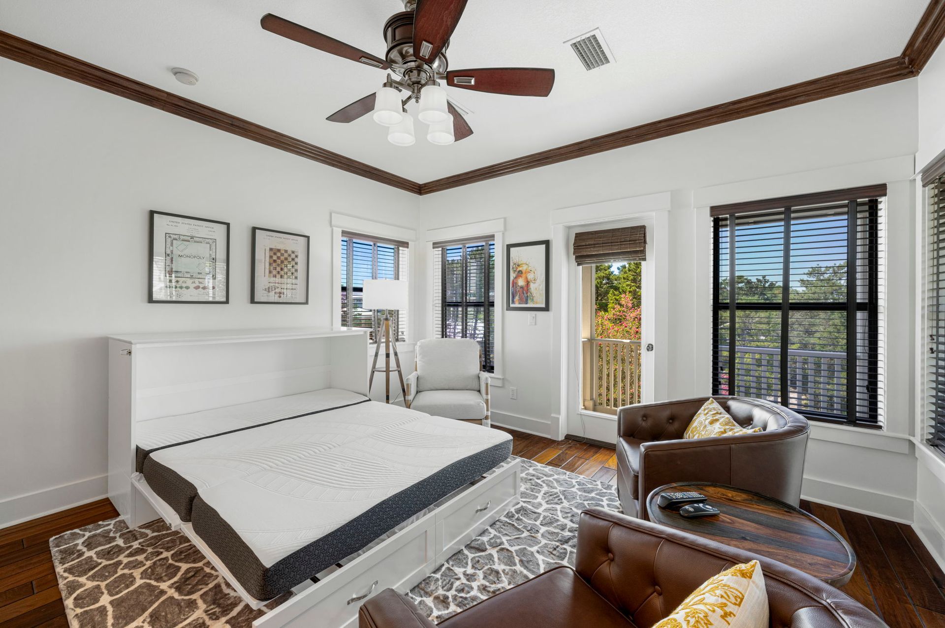 Bright bedroom with white bed, brown leather chair, patterned rug, and windows with blinds and views outside