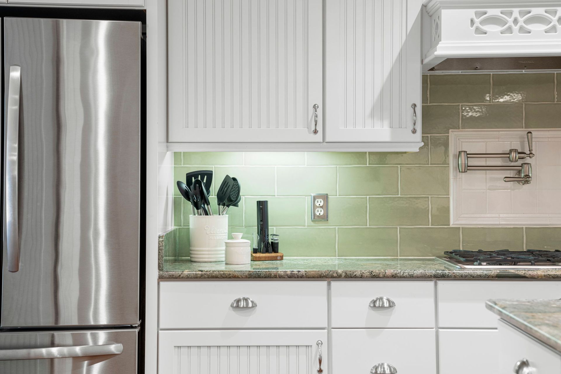 Modern white kitchen with stainless steel fridge, pale green backsplash, and countertop decor