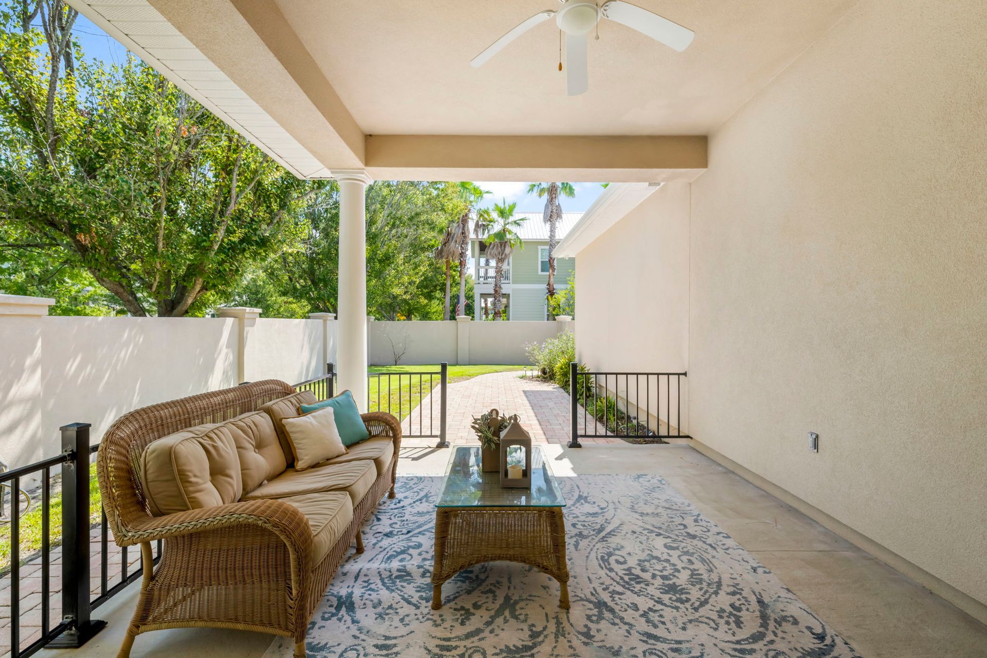 Covered patio with wicker sofa and coffee table, overlooking a green backyard and neighboring houses.