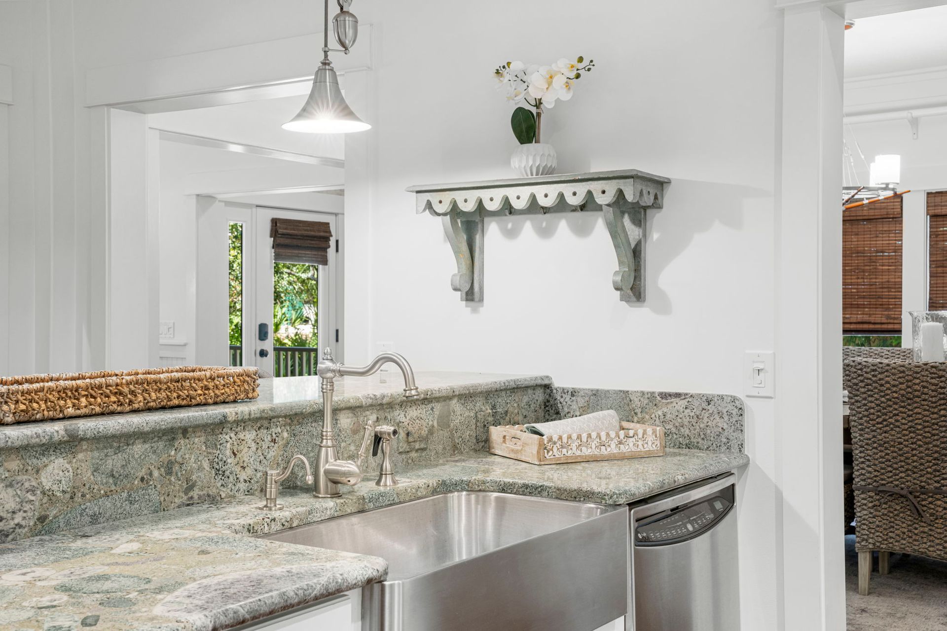 Bright kitchen with granite countertops, stainless sink, white cabinetry, and a pass-through shelf with flowers