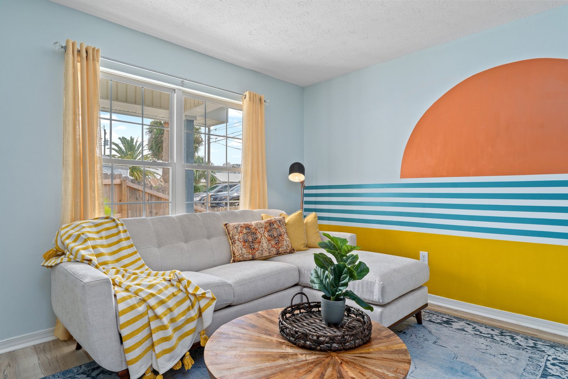 Bright living room with gray sofa, striped accent wall, yellow curtains, and round wood coffee table