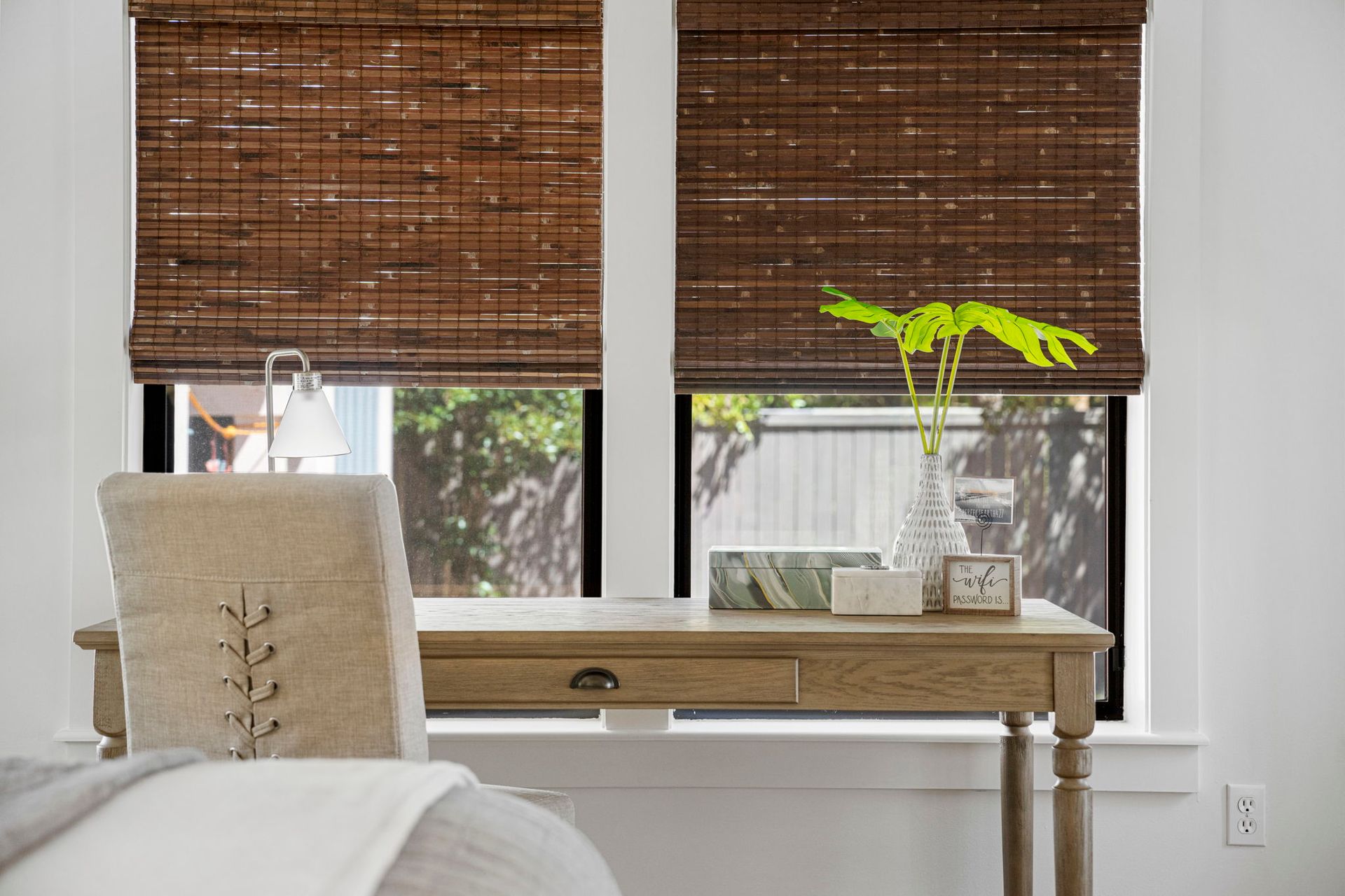 Bright home office with woven blinds, desk, chair, and a small plant by a window.
