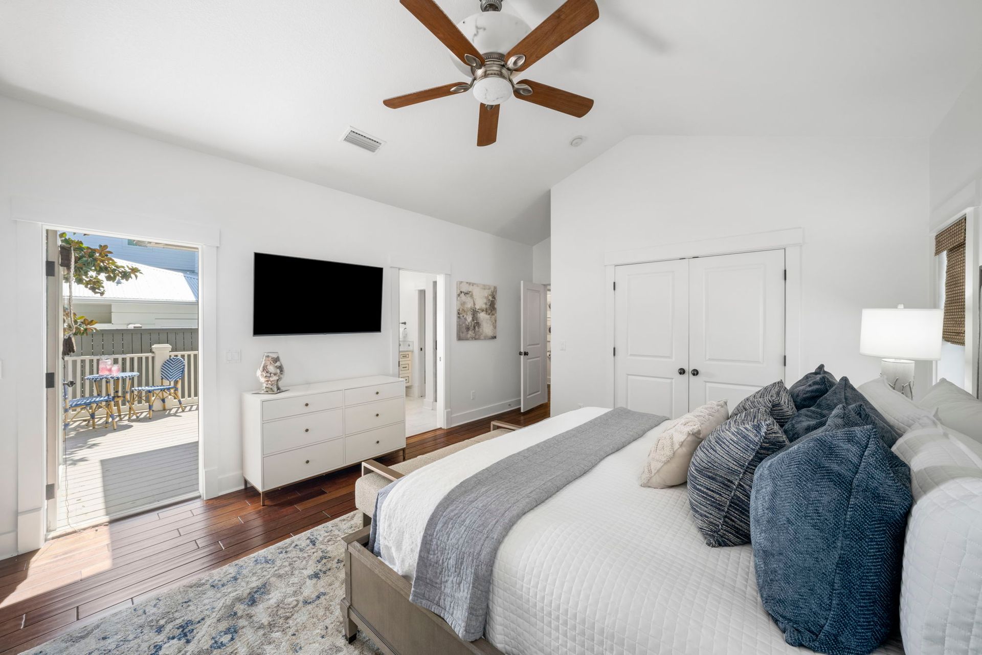 Bright modern bedroom with king bed, TV dresser, ceiling fan, and open balcony doors.