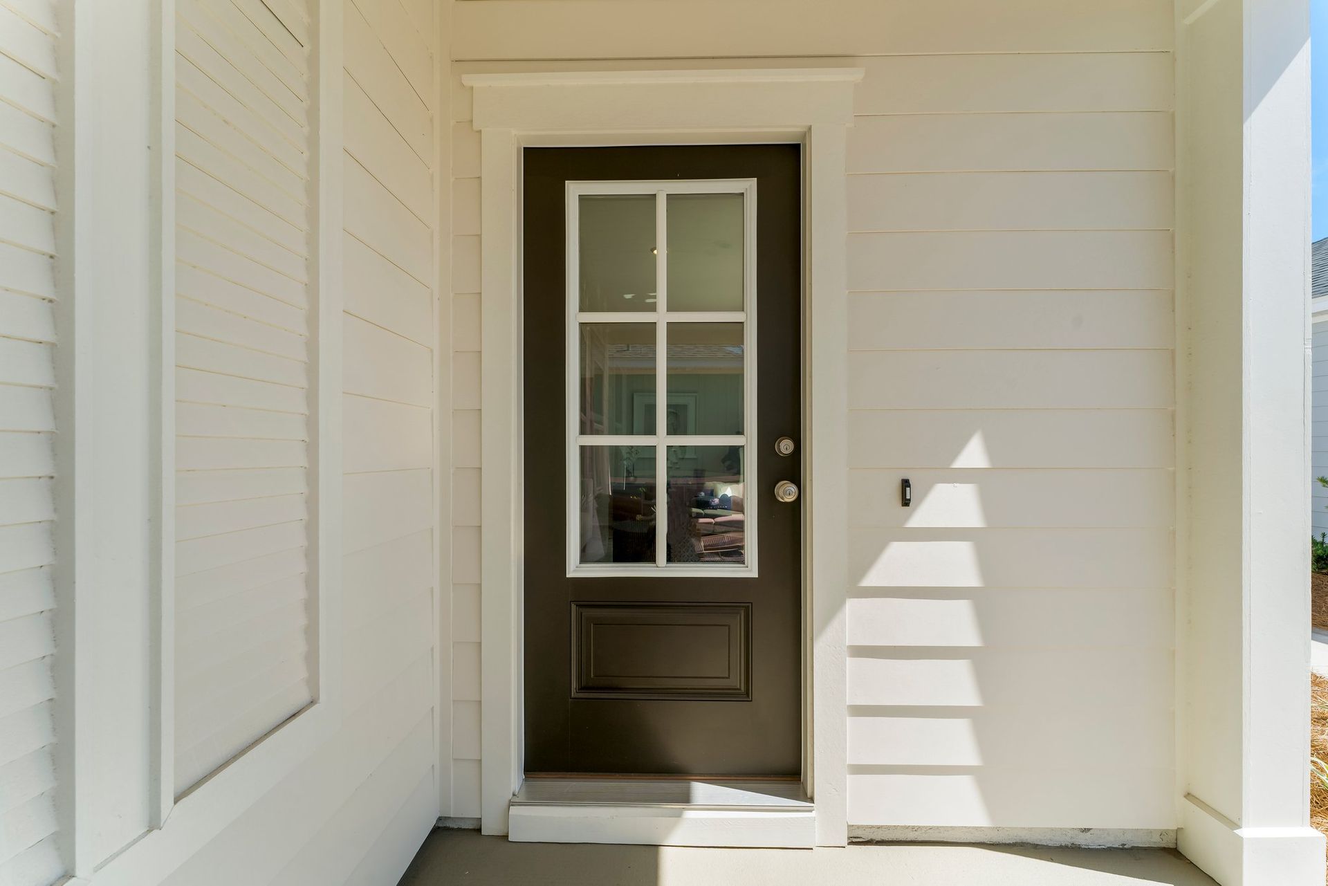 White front porch with a dark door and narrow glass panes in a bright entryway.
