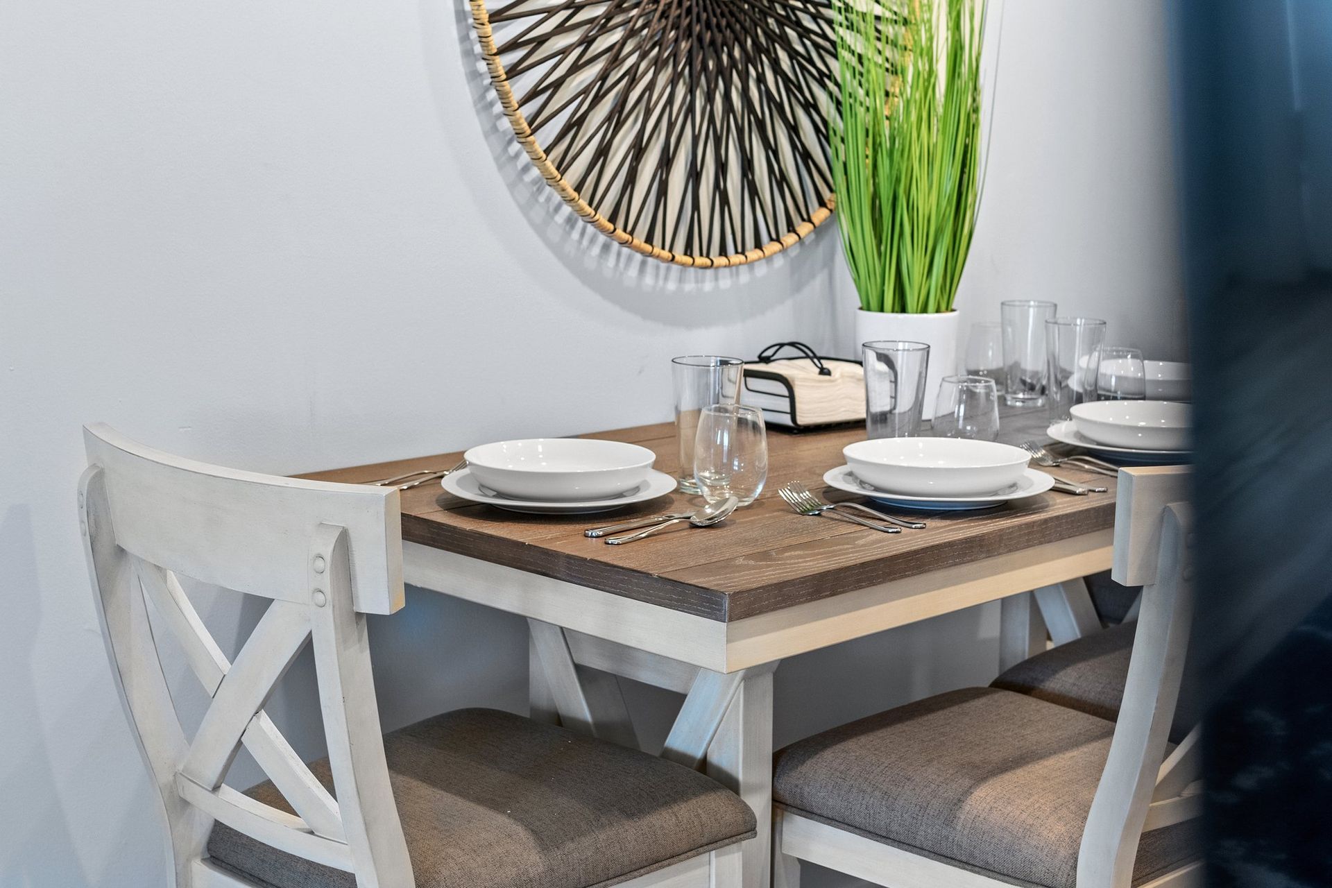 Small dining nook with wooden table, white chairs, set plates, and a round wall mirror.
