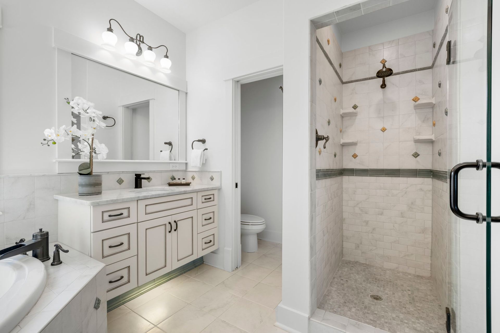 Bright white bathroom with double vanity, mirror, toilet, and tiled walk-in shower with glass door