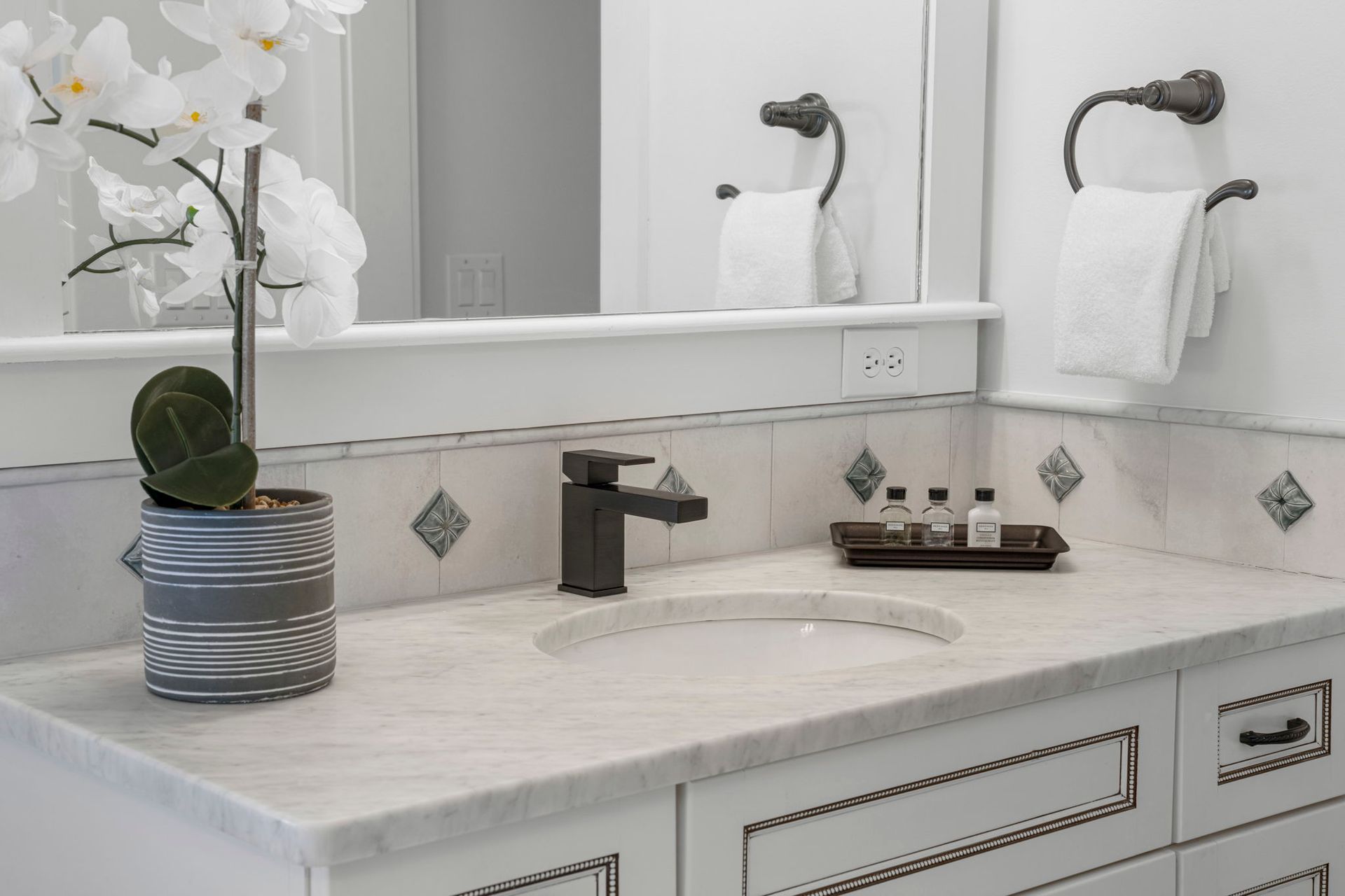 Bright bathroom vanity with white orchid, marble counter, black faucet, and mirror reflection