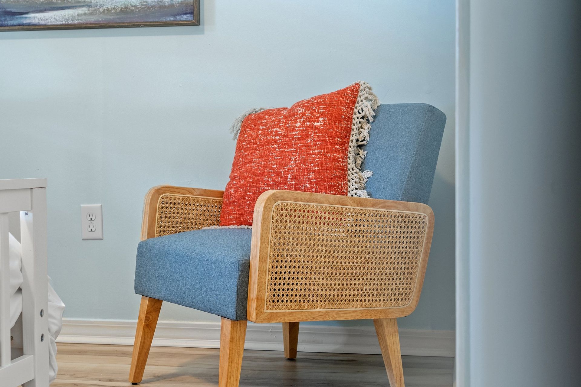 Blue upholstered armchair with wicker arms and red patterned pillow in a light blue room
