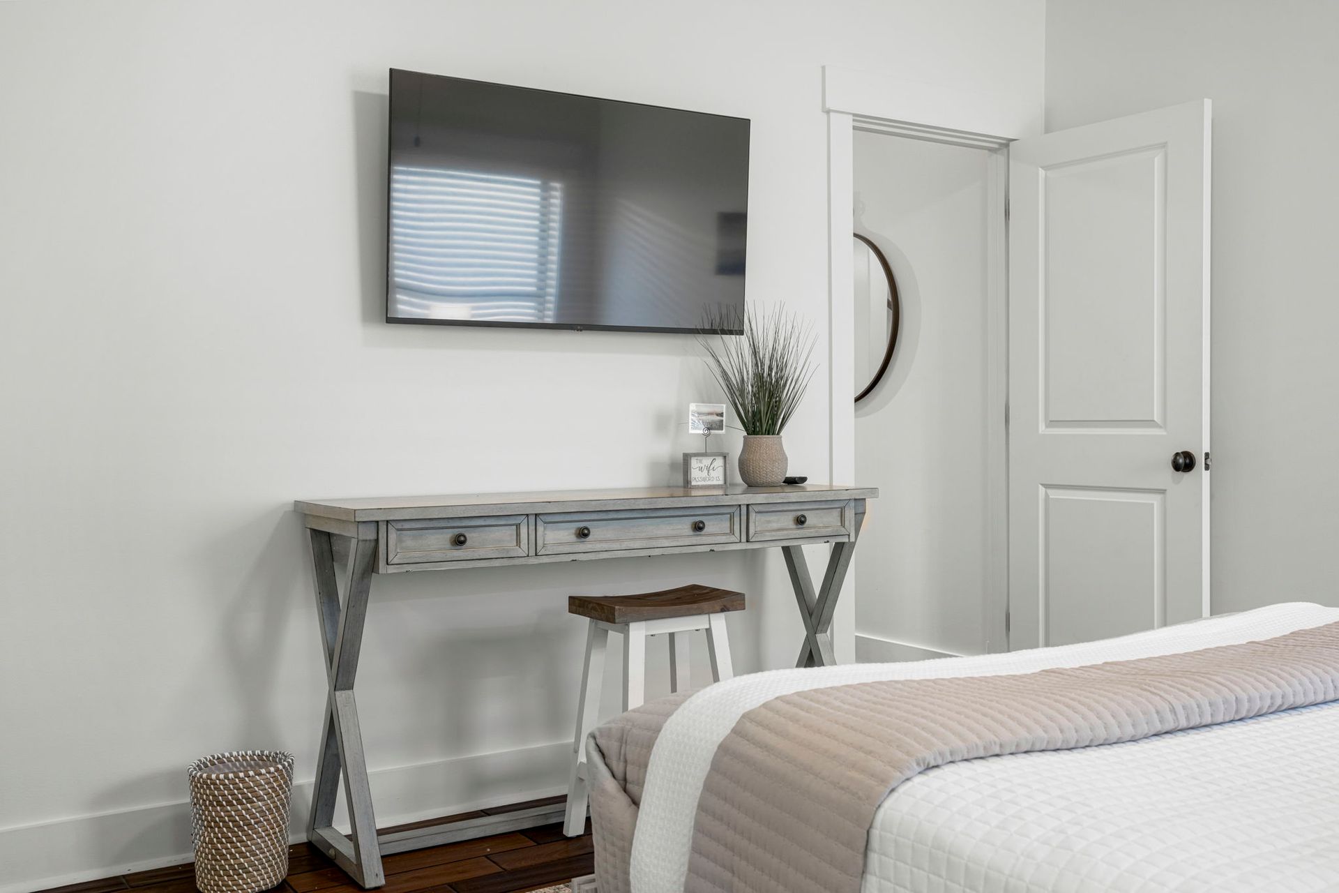 Minimal bedroom with wall-mounted TV, desk, stool, open door, and bed edge