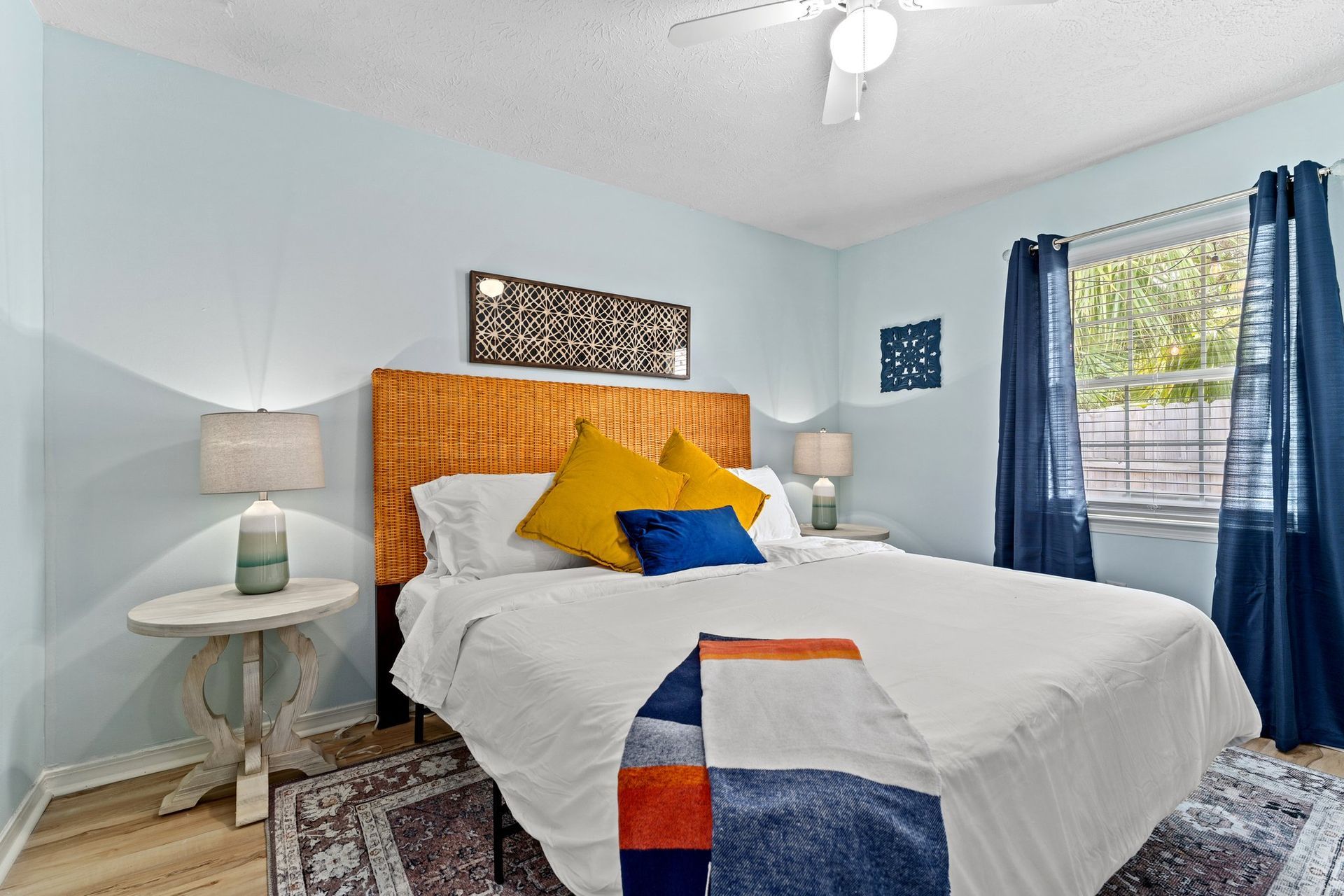 Bright blue bedroom with a white bed, orange headboard, blue curtains, and bedside table lamp
