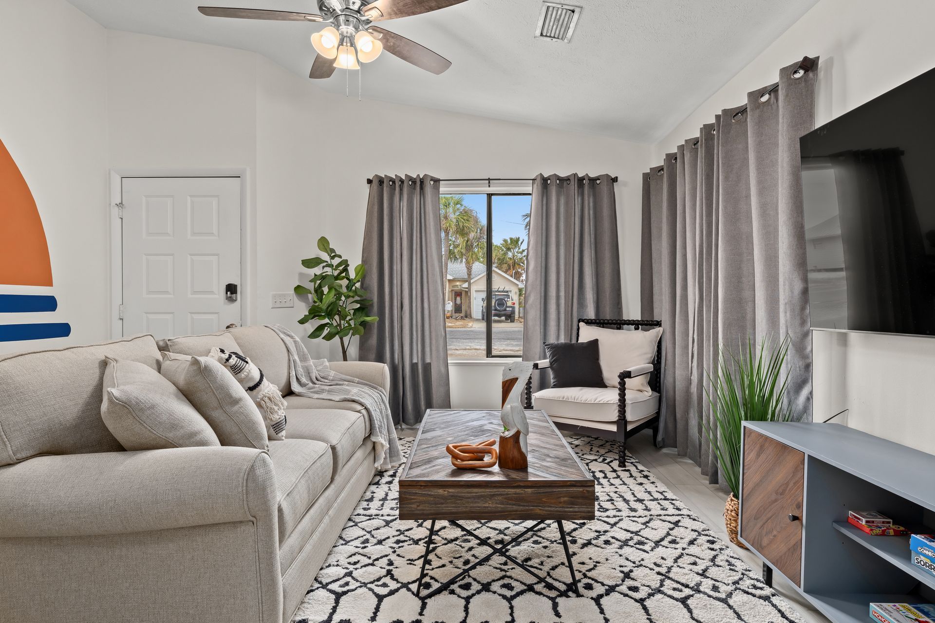 Bright living room with beige sofa, patterned rug, TV, and sliding glass doors to a balcony.