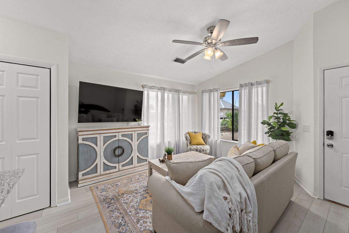 Bright living room with gray sofa, TV console, rug, and bay windows with natural light