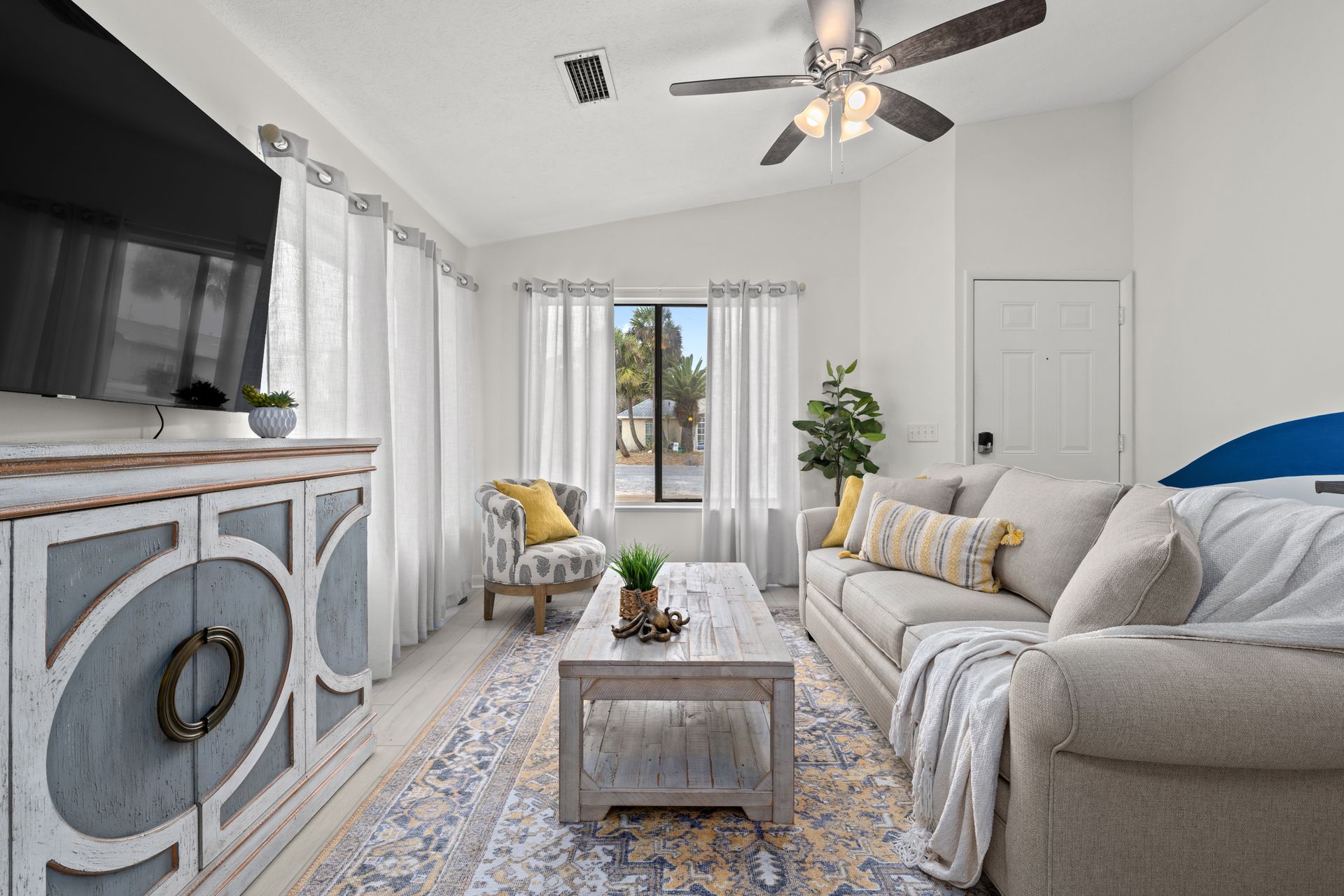 Bright living room with white sofa, patterned rug, TV, fireplace, and balcony doors with sheer curtains.