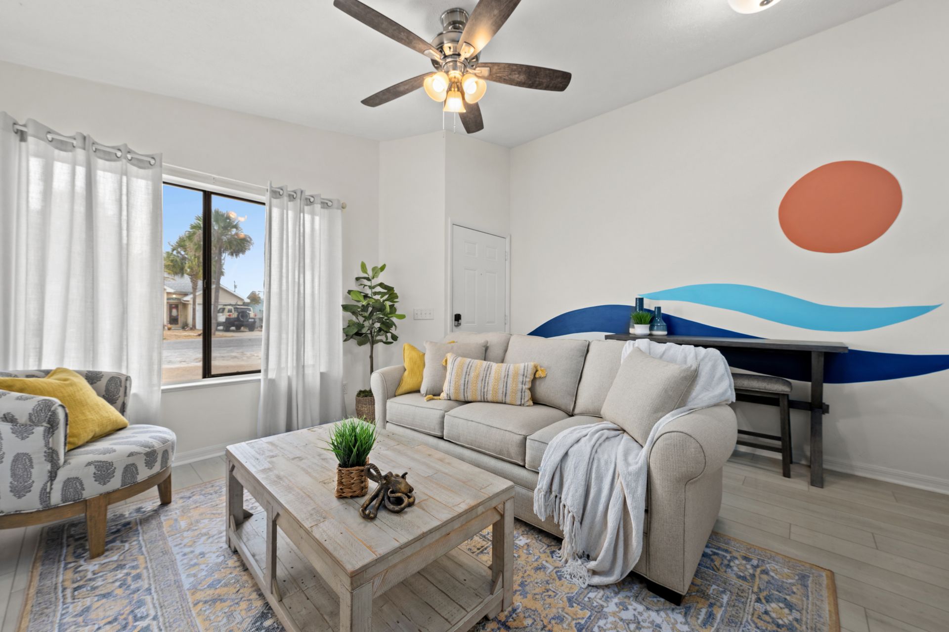 Bright living room with white sofa, patterned chair, coffee table, and surfboard wall art