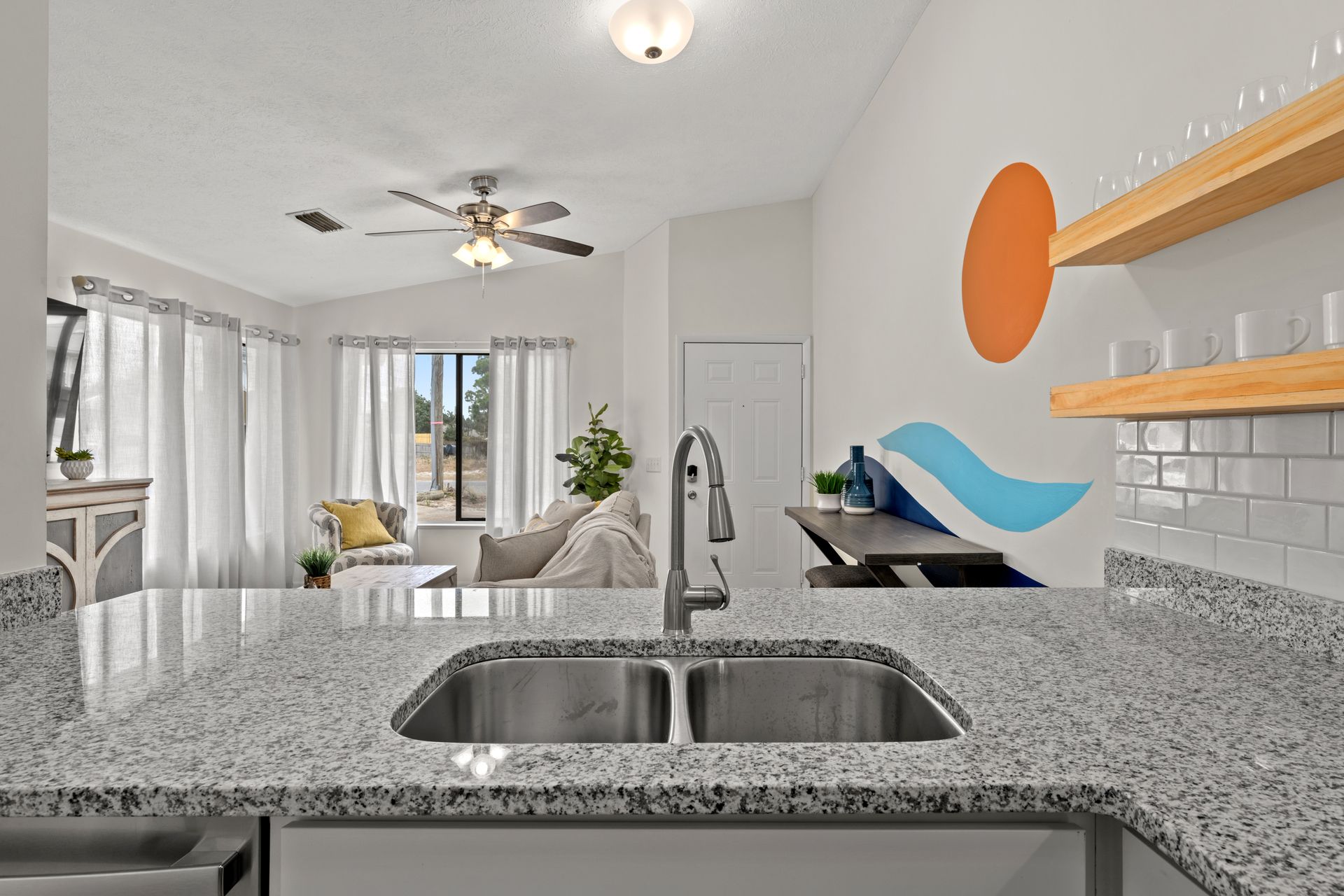 Bright modern kitchen looking into a white living room with granite island and orange wall art