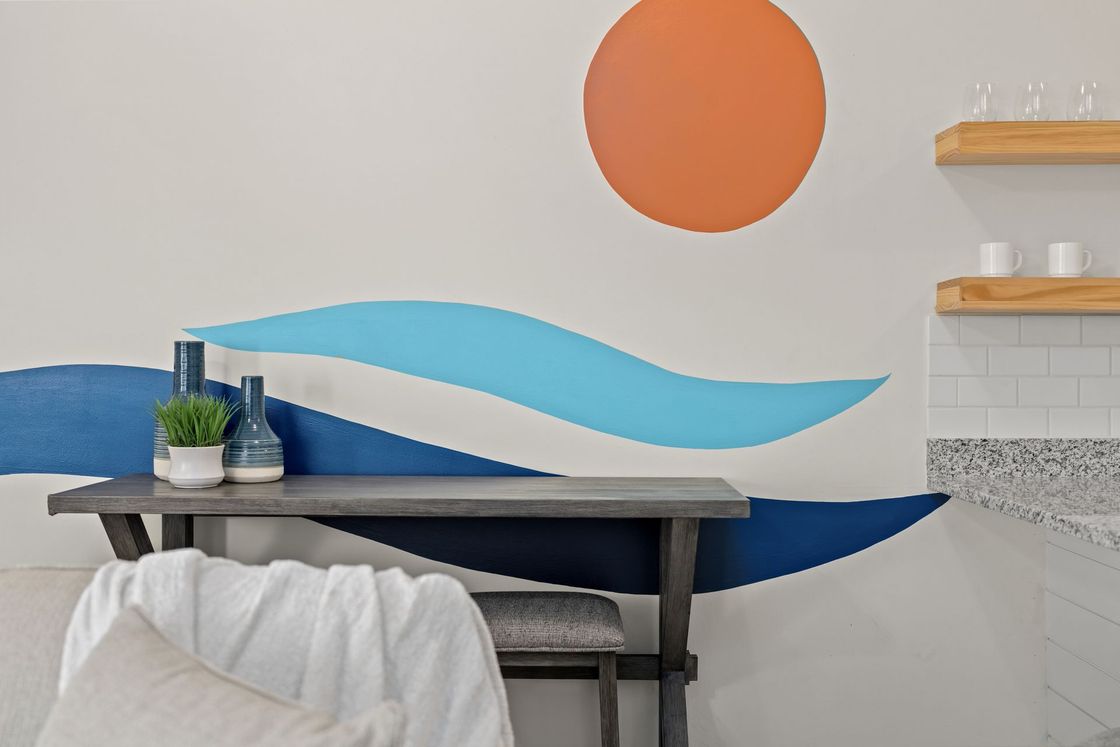 Modern room with blue wave wall mural, orange sun circle, desk, and chair