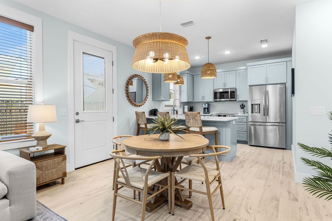 Bright modern kitchen-dining area with round wooden table, wicker chairs, and stainless steel appliances