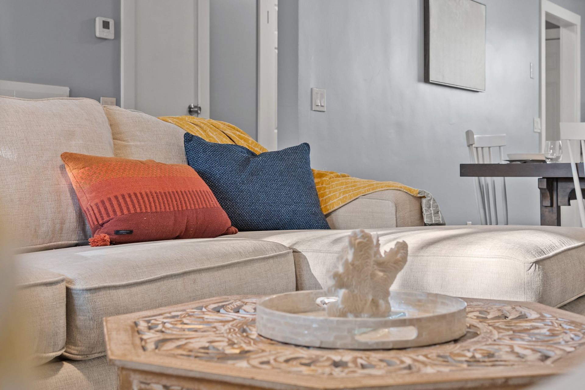 Cozy living room with a beige sofa, colorful pillows, and a wooden coffee table with a decorative bowl.