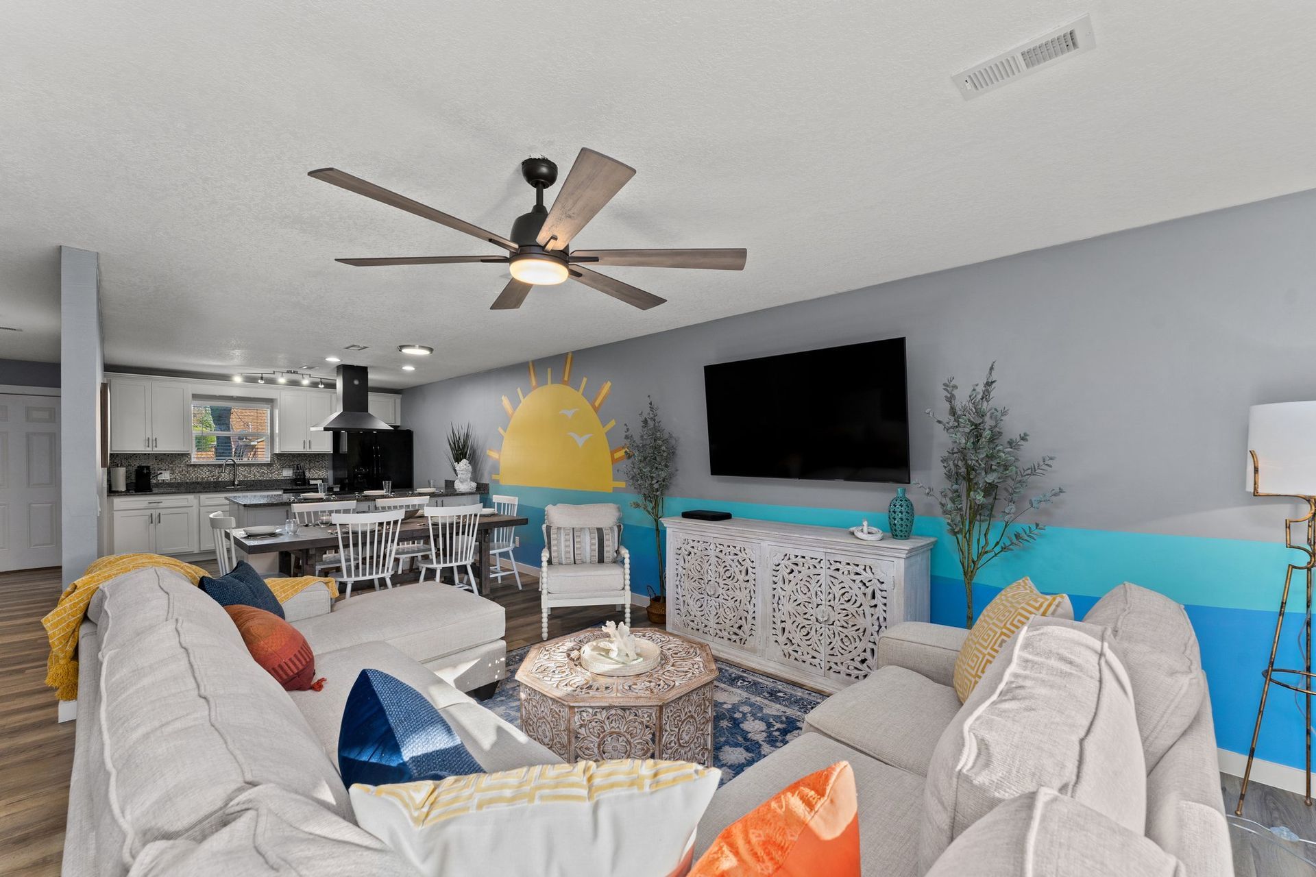 Bright open living room with white sectional, TV, ceiling fan, and yellow accent chair