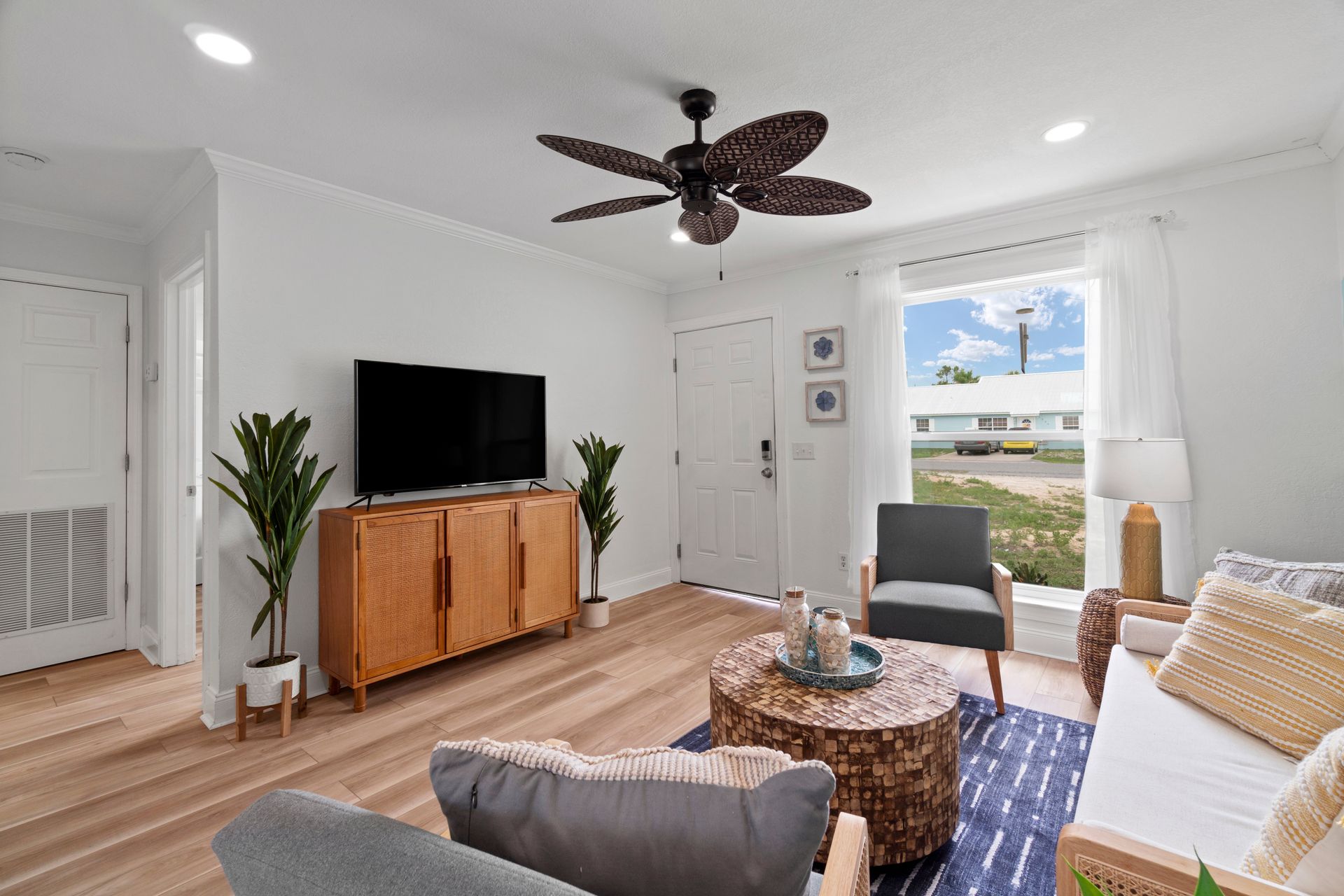 Bright living room with TV, wood console, ceiling fan, and open door to a sunny balcony.