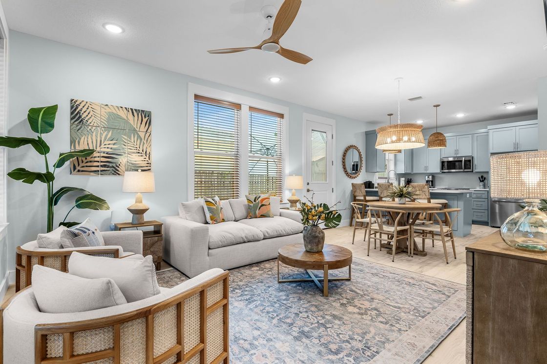 Bright, modern living-dining room with white sofa, wood dining table, large windows, and coastal decor