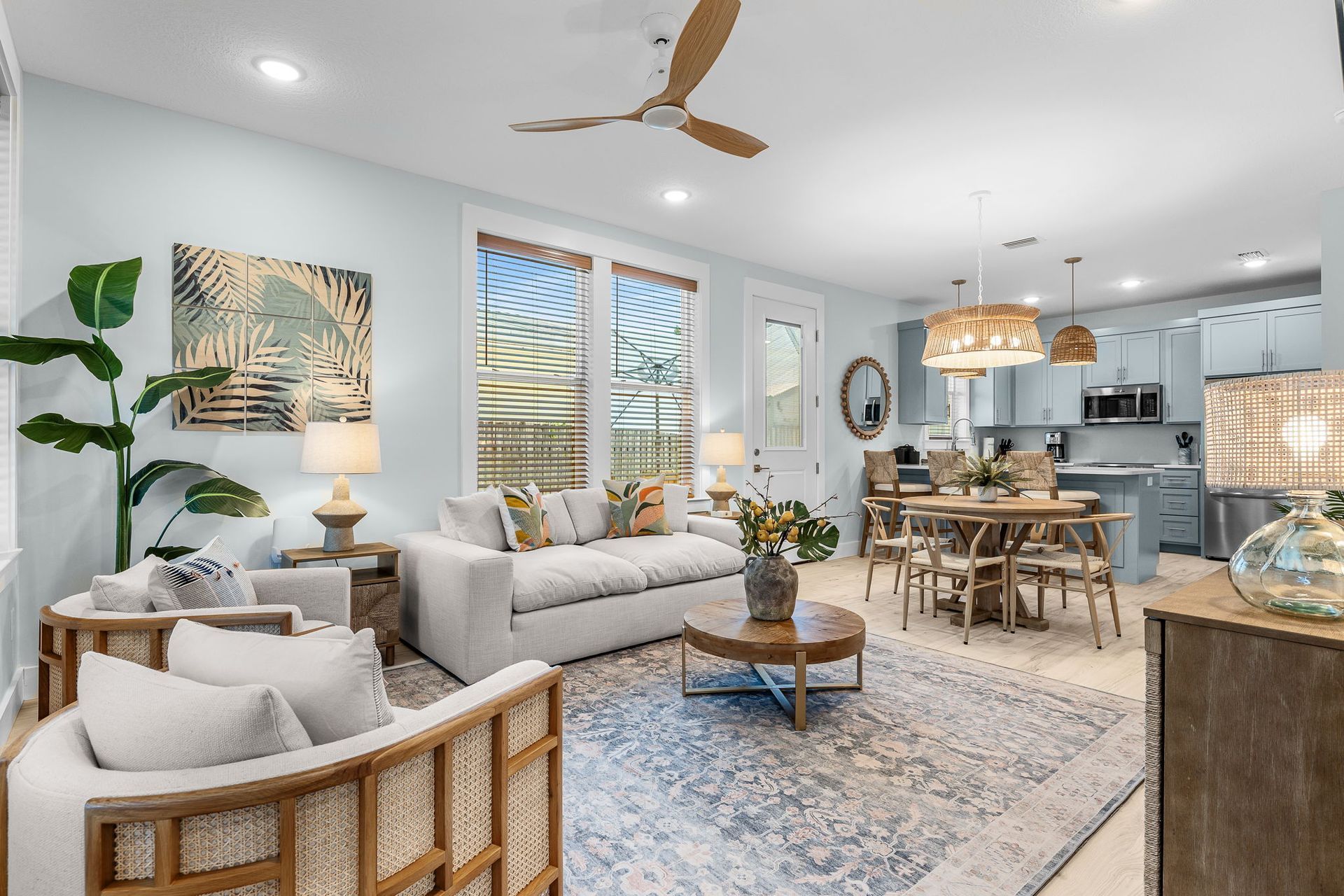 Bright, modern living-dining room with white sofa, wood dining table, large windows, and coastal decor