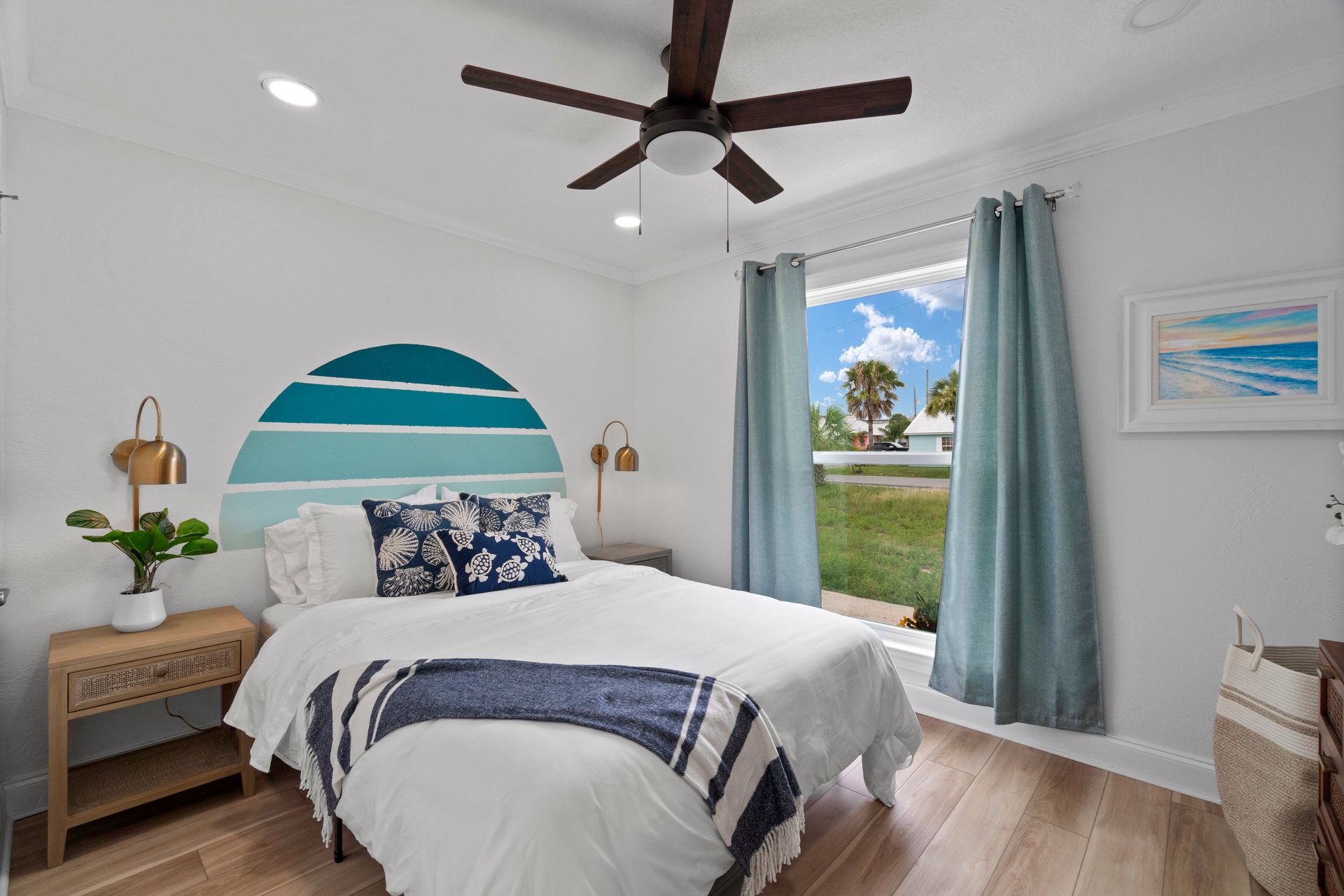 Bright bedroom with blue accents, striped bed, ceiling fan, and open curtains looking out to a grassy view.