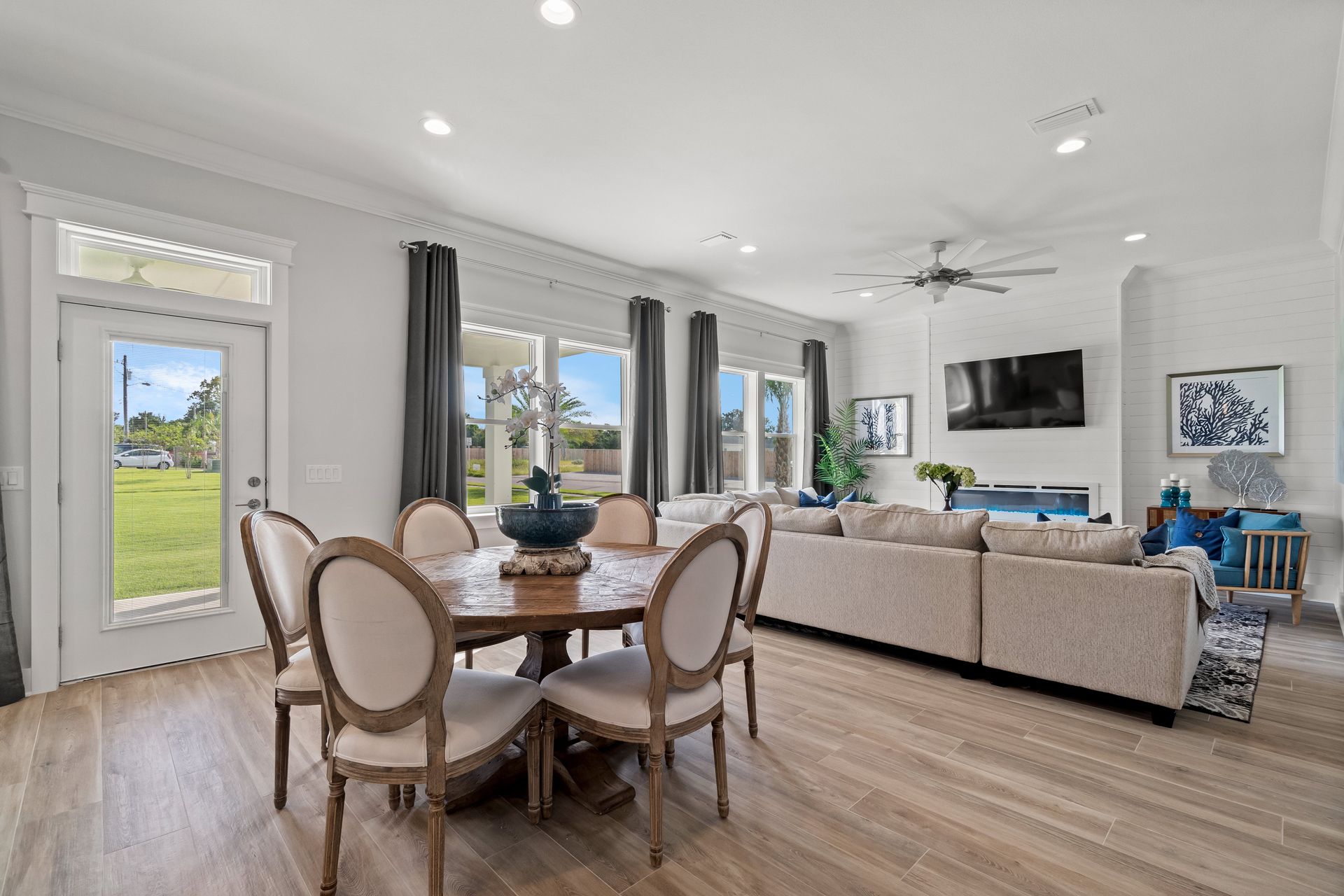 Bright open living and dining room with beige sofas, round wood table, large windows, and wall-mounted TV