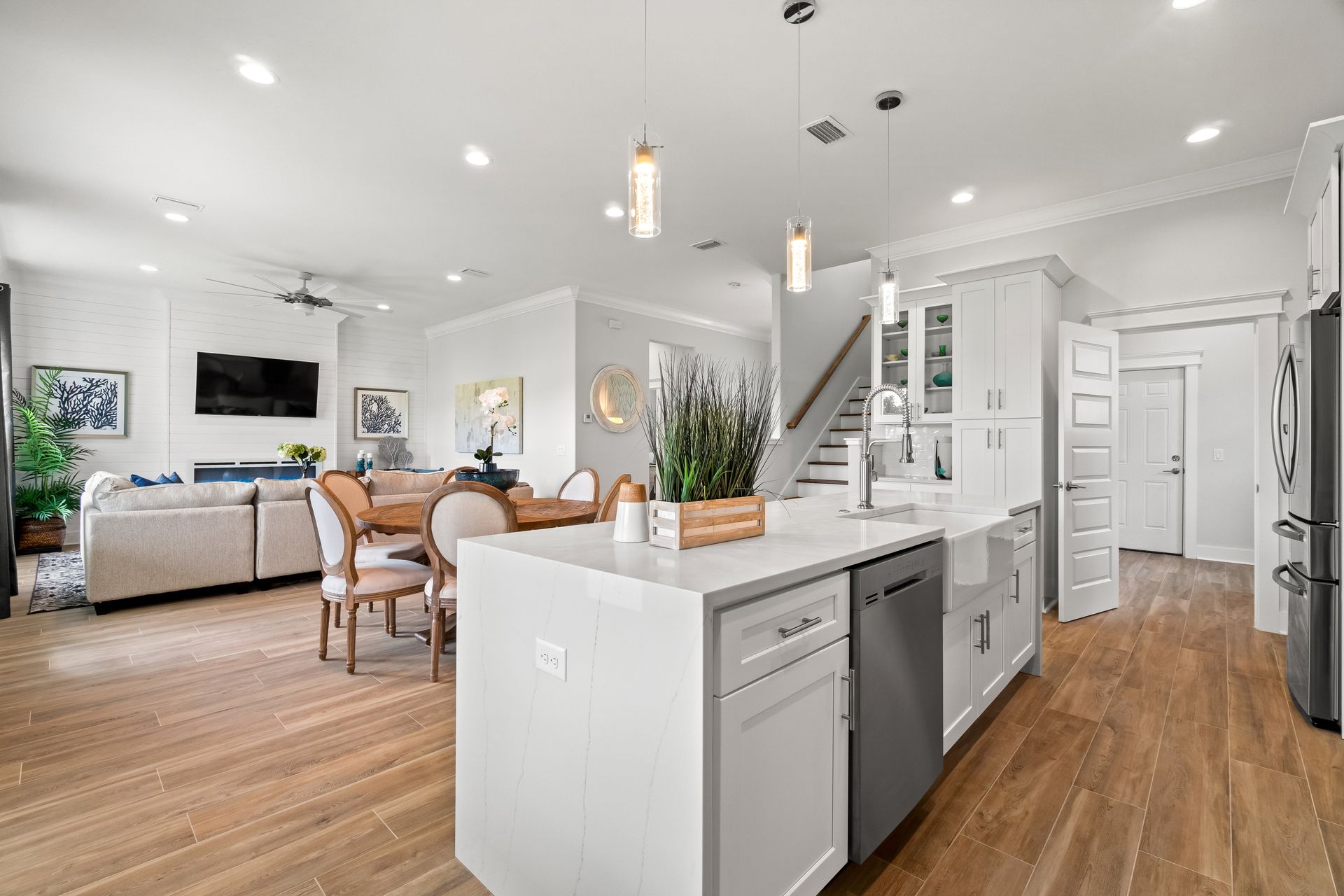 Bright open-concept kitchen and dining area with white cabinets, wood floors, and gray sofa in the background