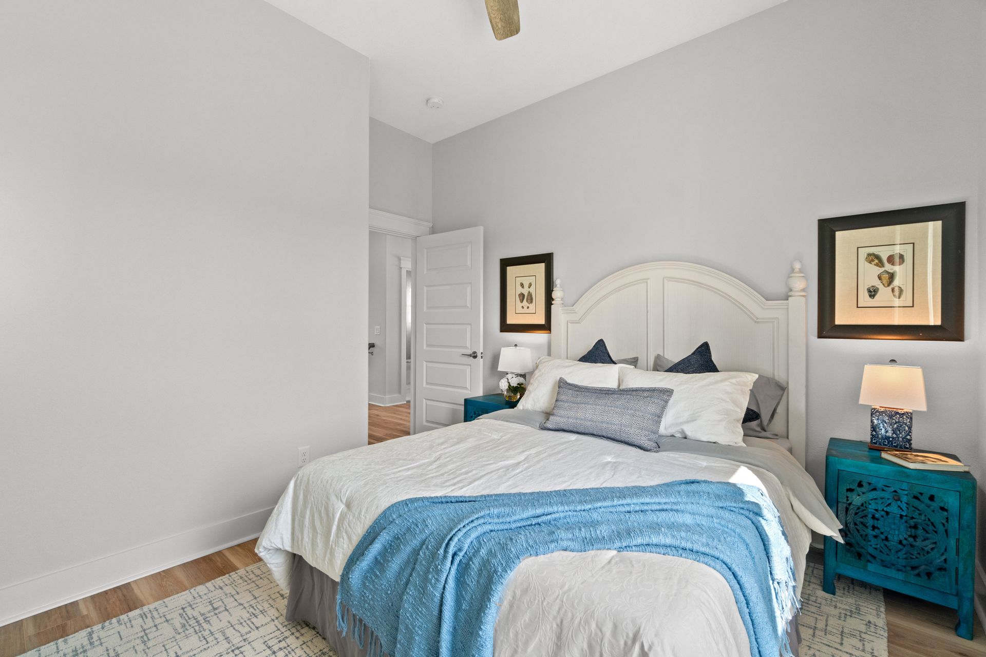 Bright bedroom with white bed, blue blanket, teal nightstand, and light gray walls