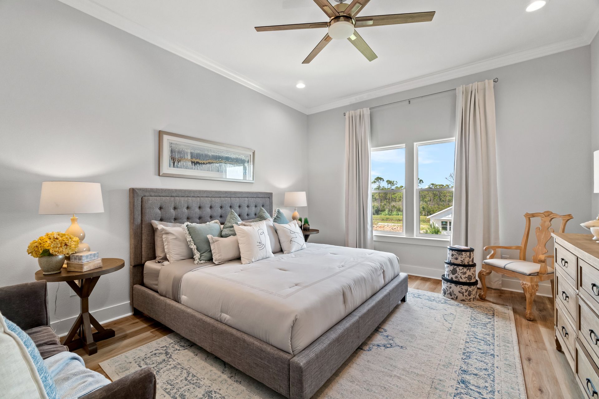 Bright bedroom with a gray bed, window view, ceiling fan, and neutral decor