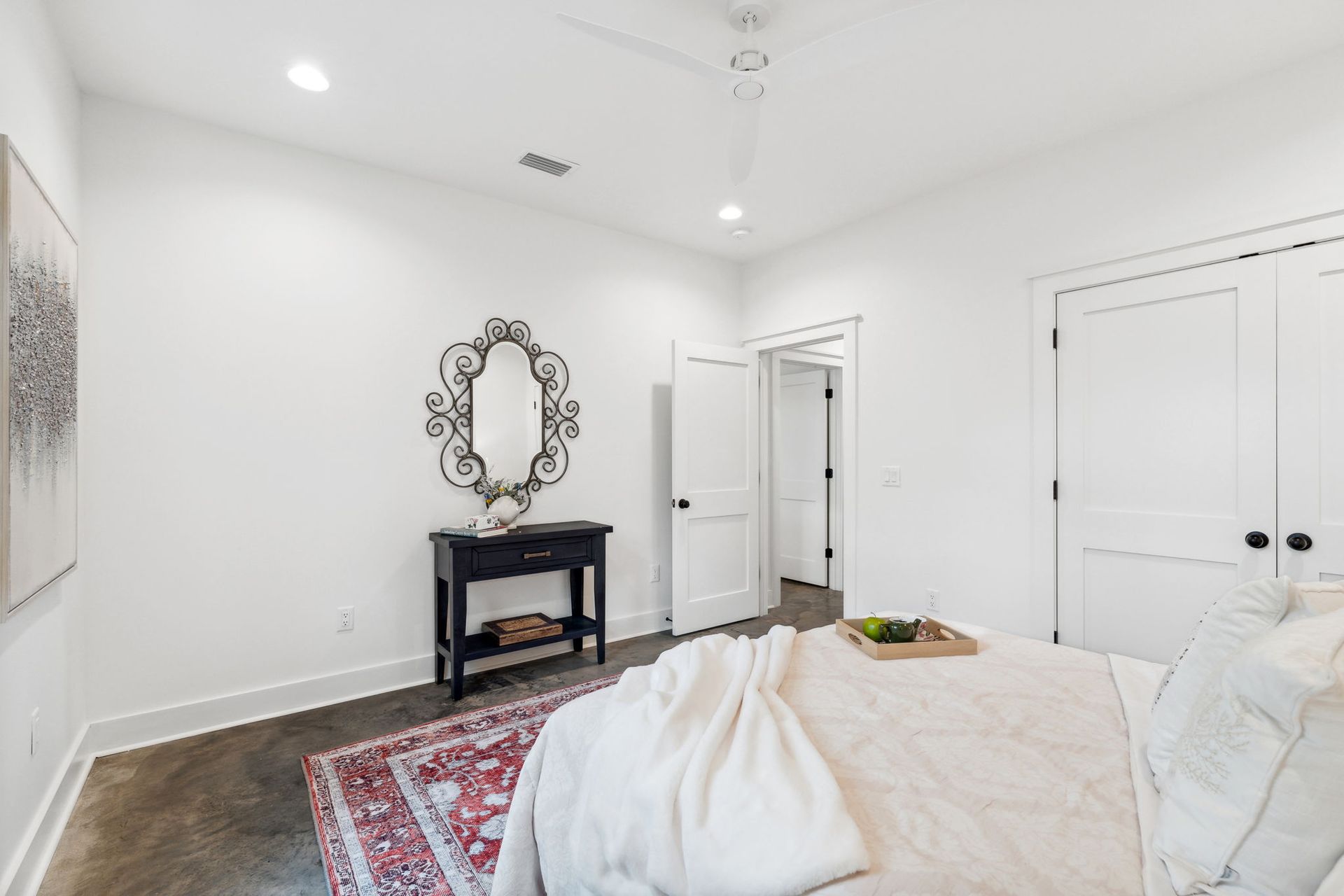 Bright bedroom with white walls, bed, dresser, ornate mirror, and patterned rug