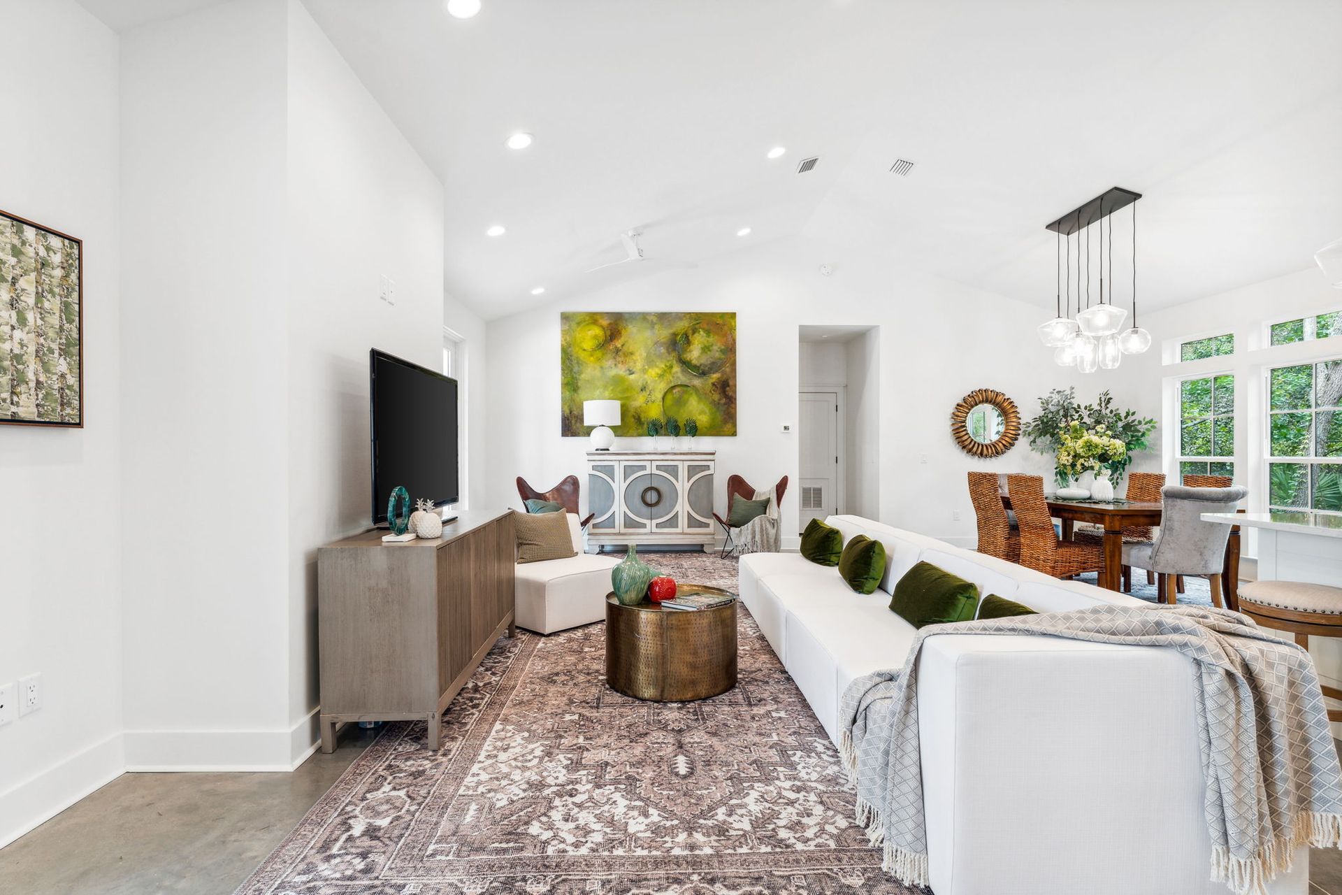 Bright living room with white walls, patterned rug, sofa, TV, and dining area by large windows