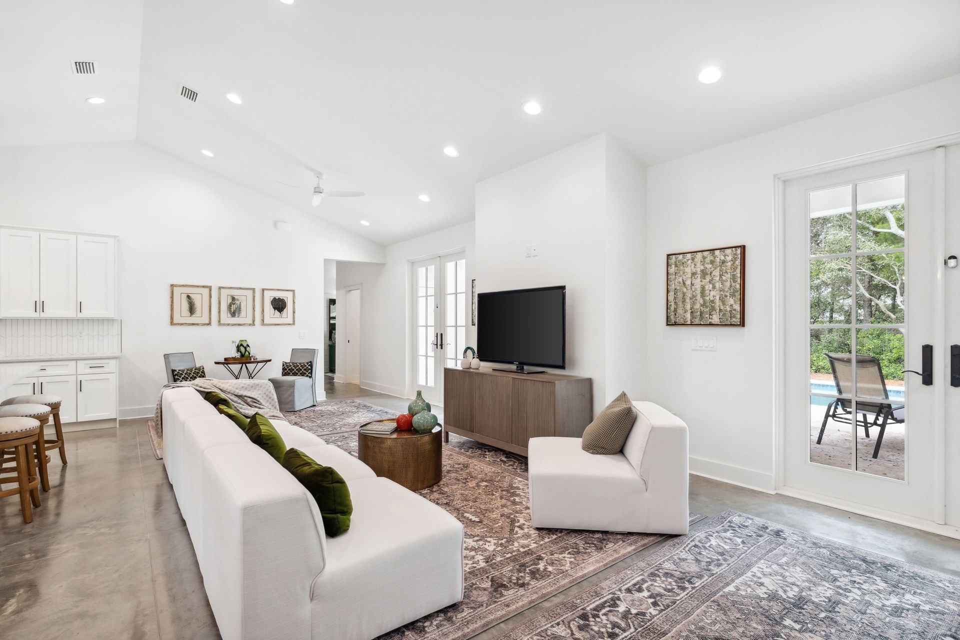 Bright modern living room with white sofas, TV, patterned rug, and patio doors letting in natural light