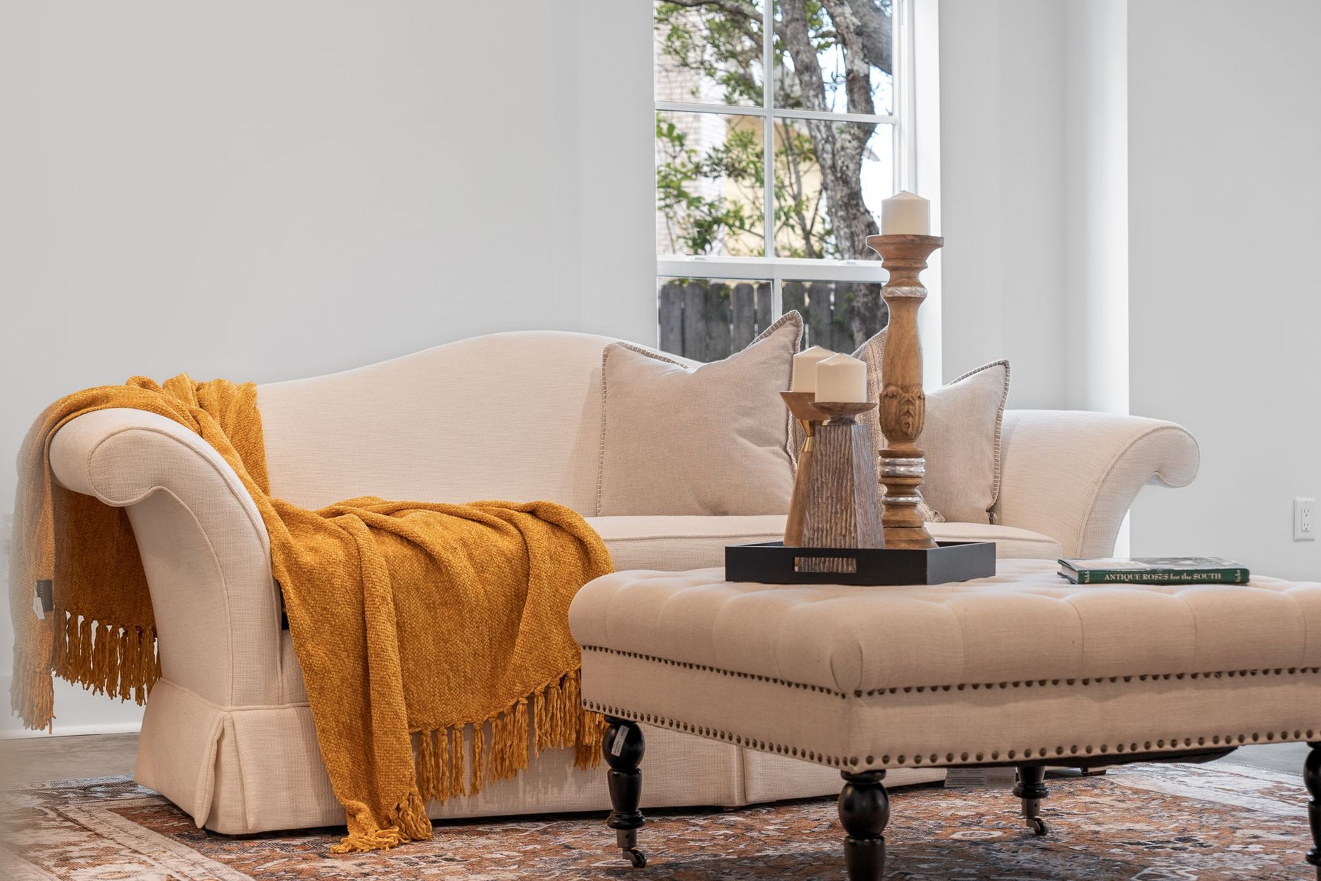 Cozy living room with beige sofa, mustard throw, ottoman, and candle decor by a window