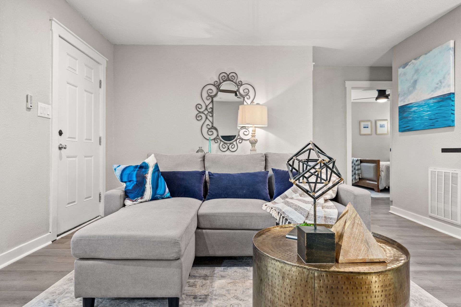 Bright living room with gray sectional, blue accents, gold coffee table, and wall mirror