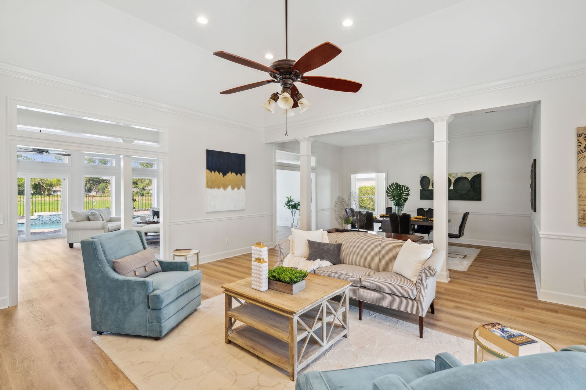 Bright modern living room with blue chairs, white sofa, wood floors, and ceiling fan