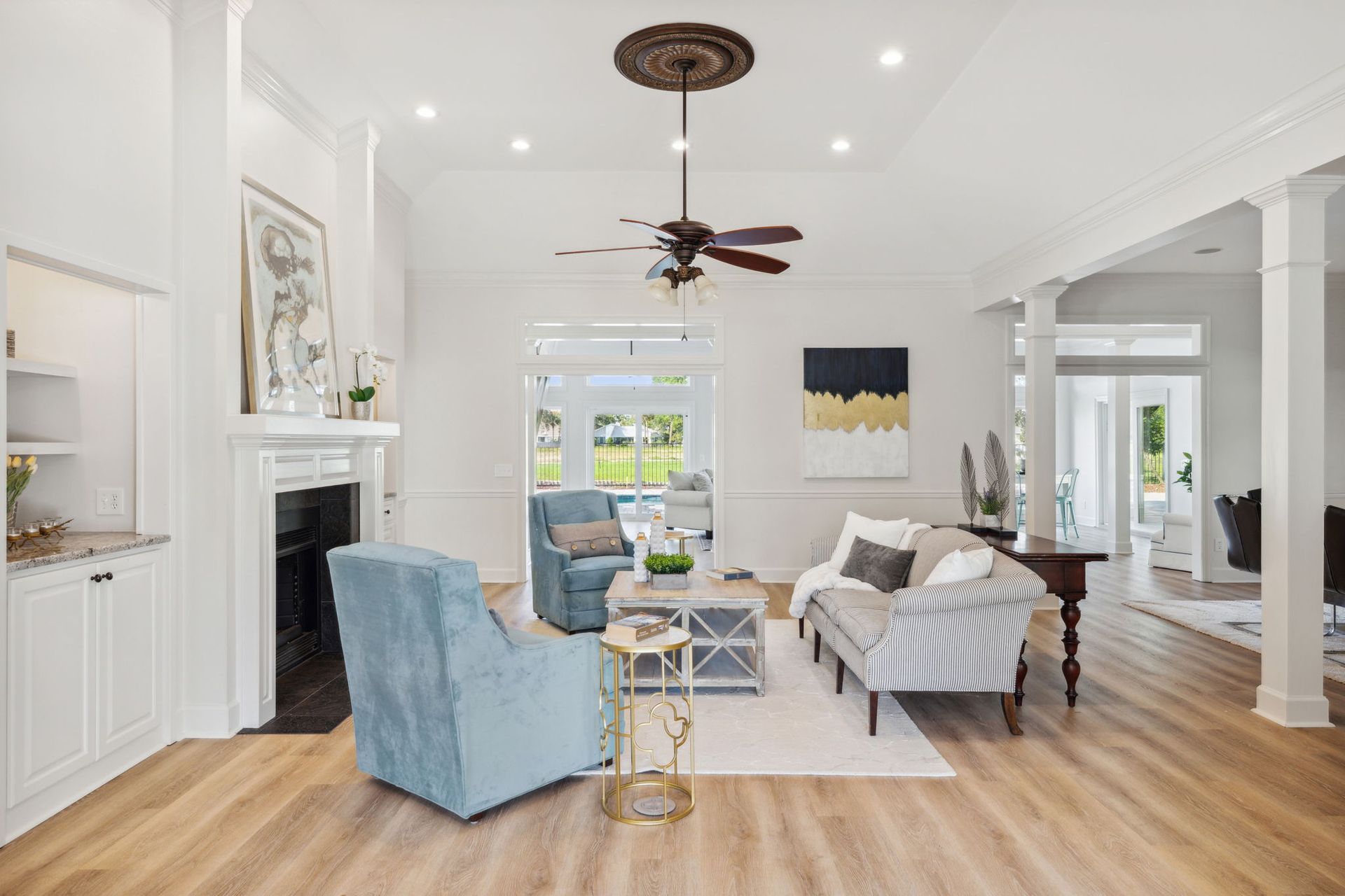 Bright living room with blue chairs, white sofa, fireplace, and ceiling fan on wood floors