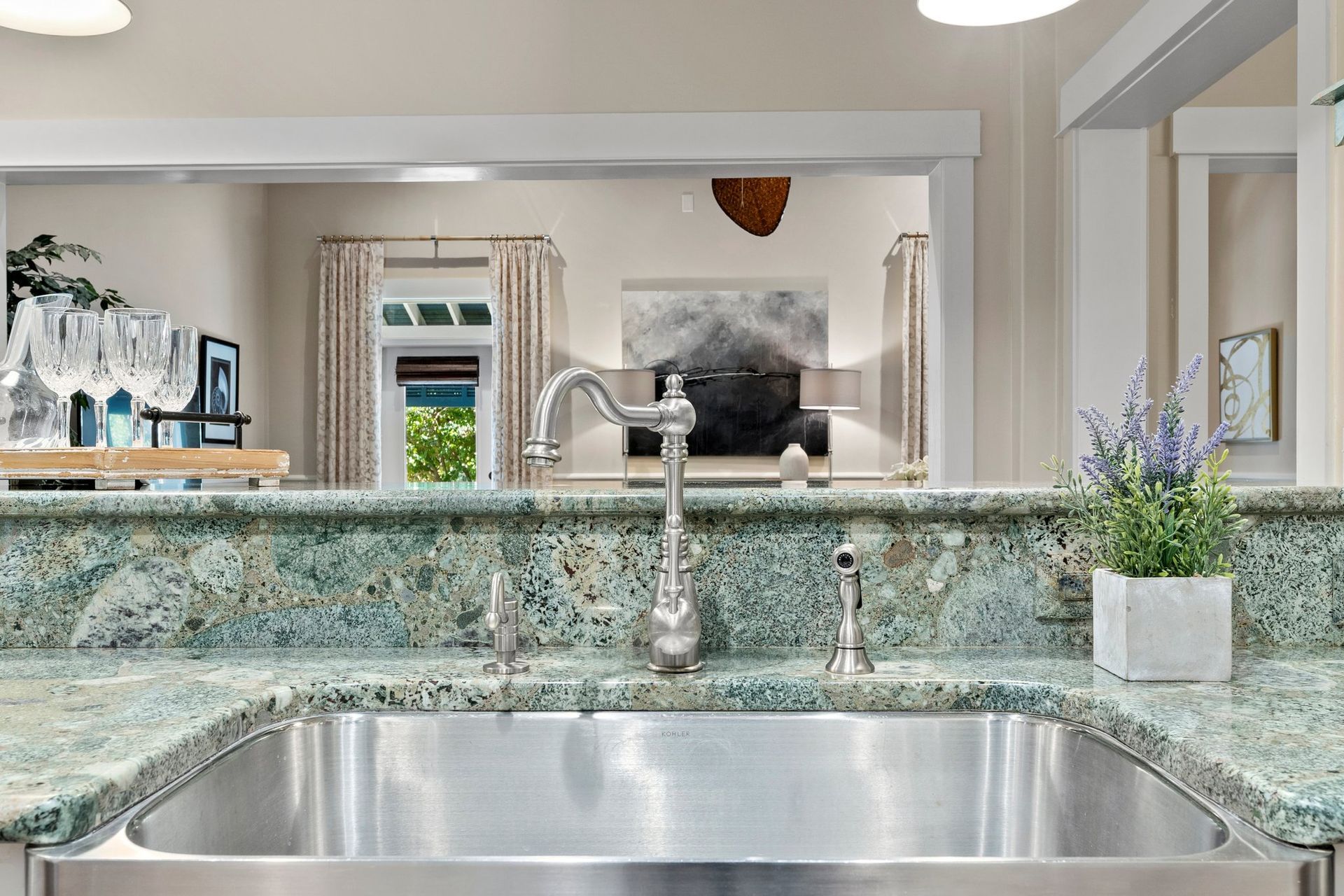 Kitchen view over granite counter and stainless sink, reflecting a dining room and window beyond.
