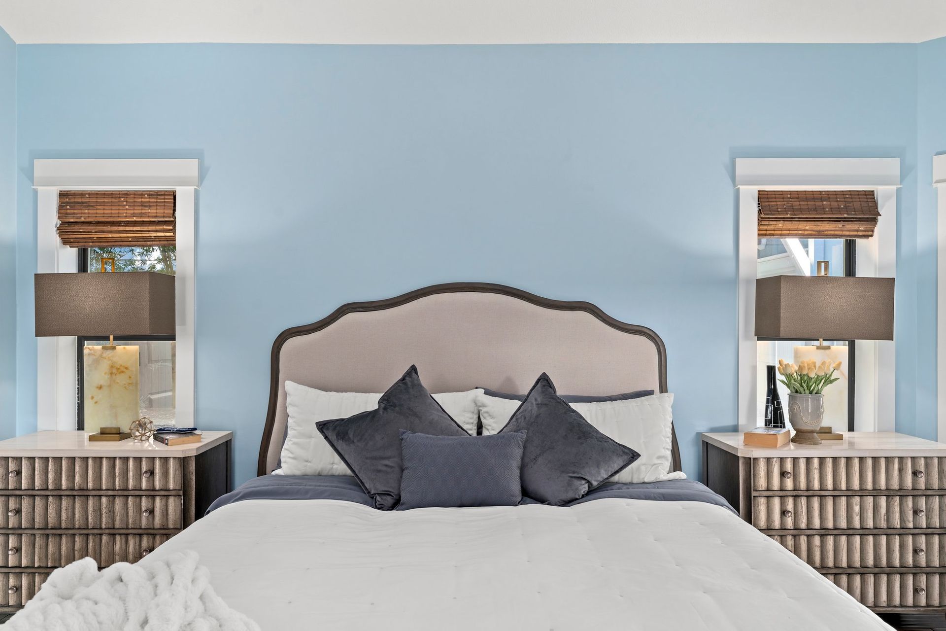 Coastal-style bedroom with a gray upholstered bed, blue walls, and matching bedside lamps.