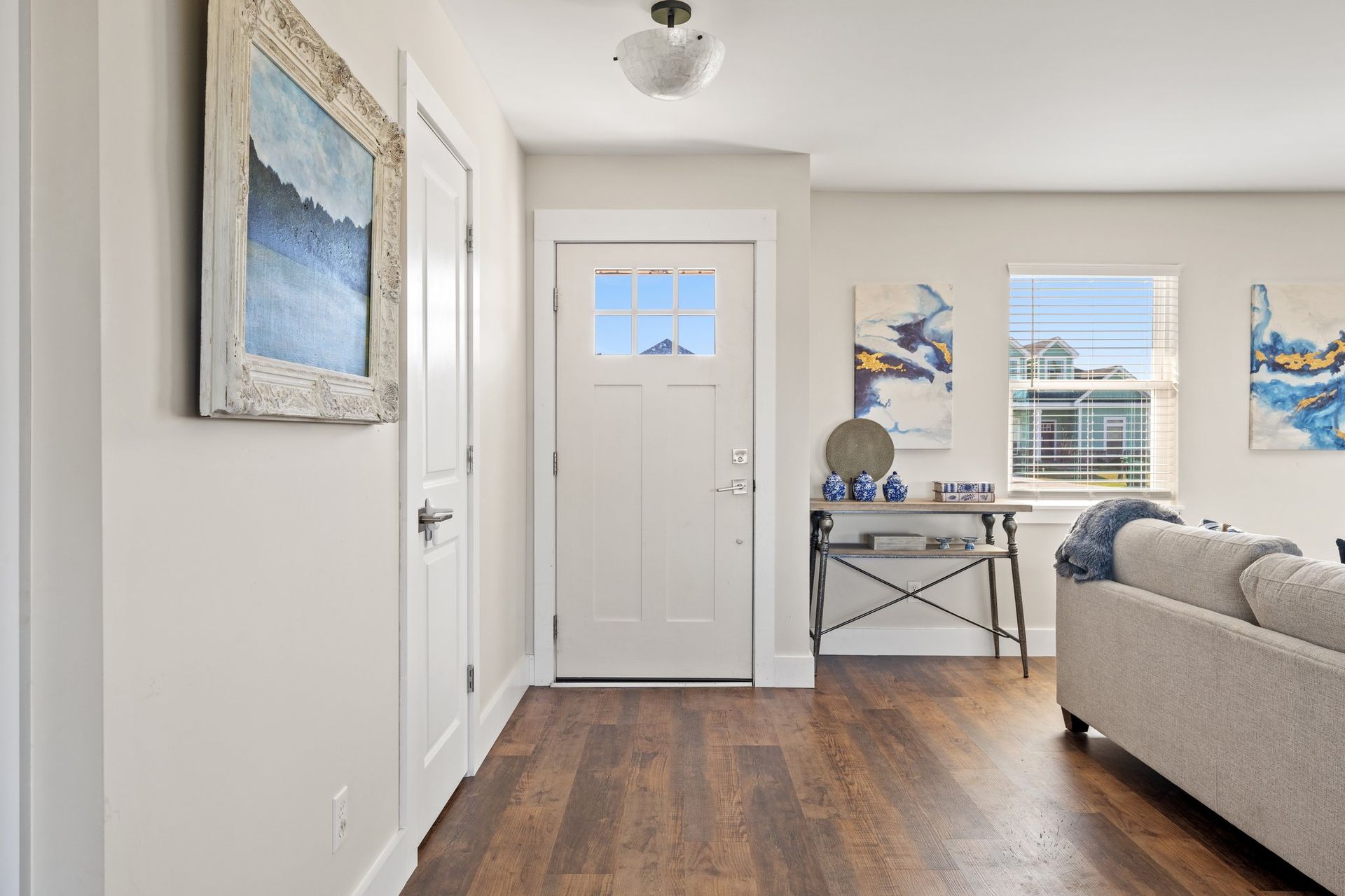 Bright hallway and living room with white walls, wood floors, and ocean-themed wall art