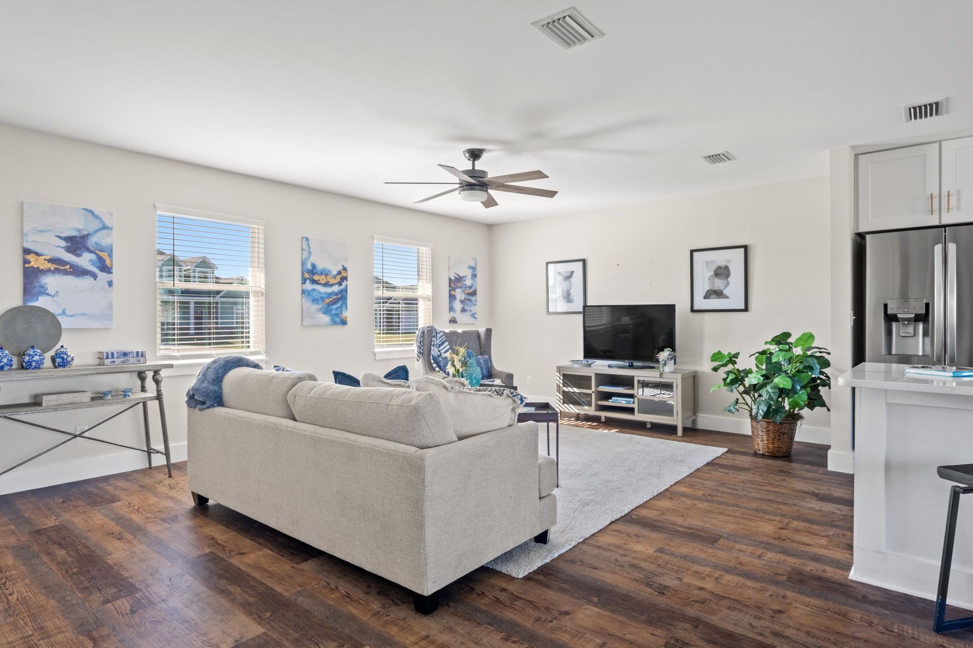 Bright open living room with gray sofa, white TV stand, hardwood floors, and kitchen view