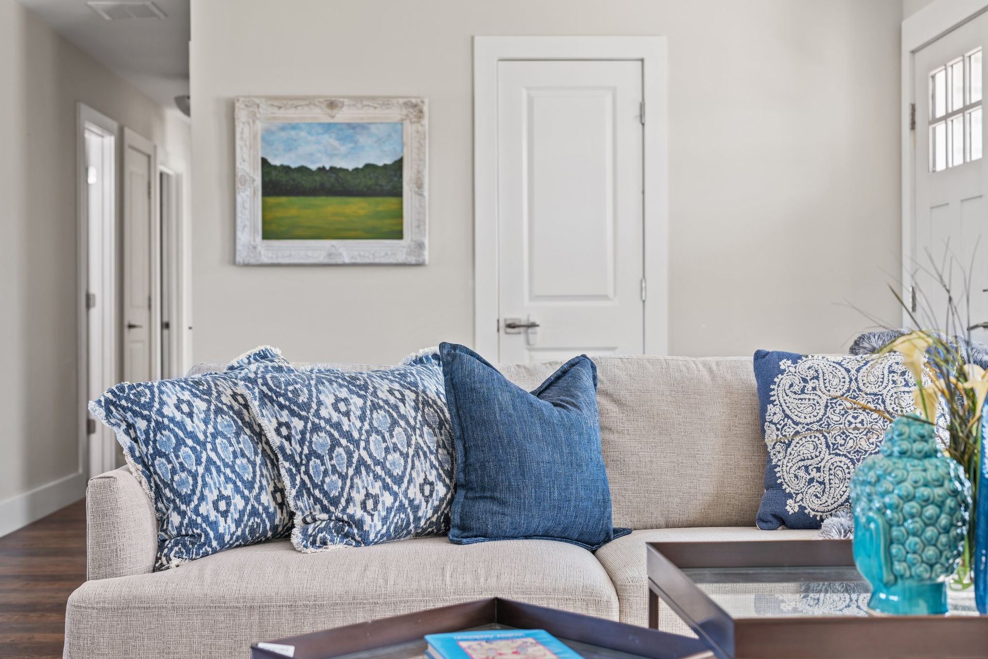 Bright living room with a beige sofa, blue patterned pillows, and a framed landscape on the wall