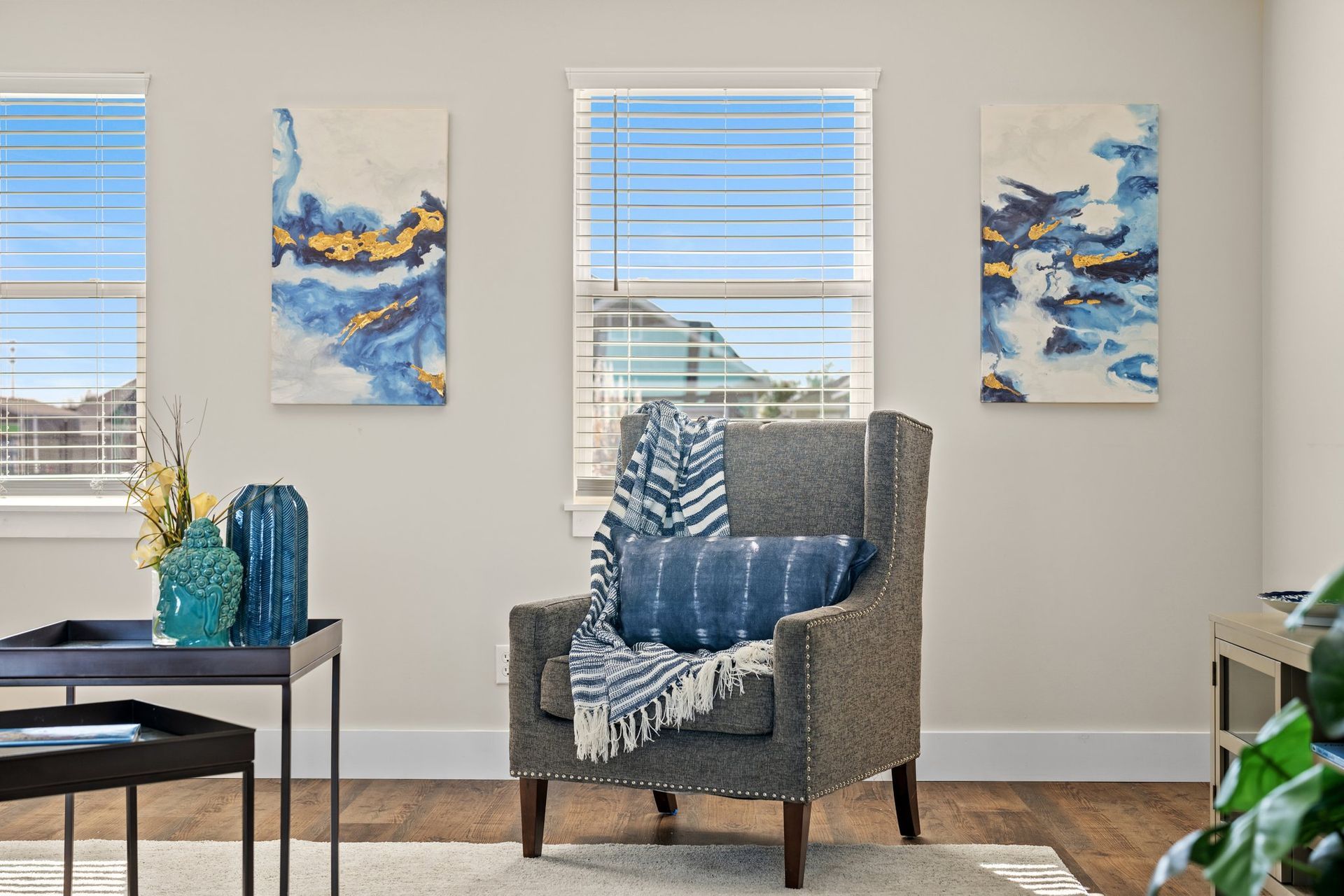 Cozy living room with gray chair, blue pillows, abstract wall art, and sunlight through windows