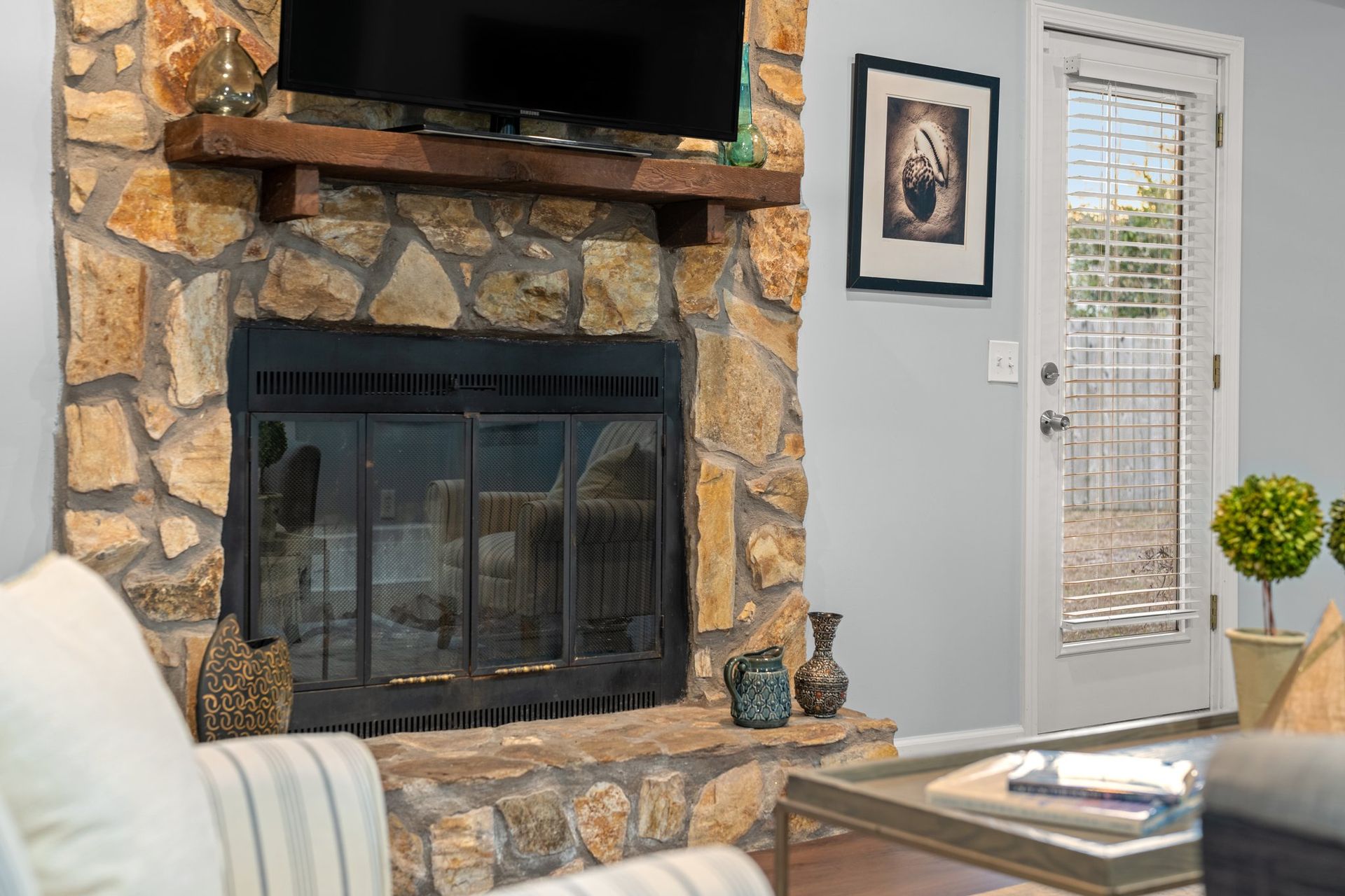 Living room fireplace with stone surround, mounted TV, and glass door to the right
